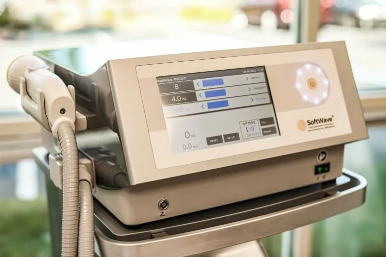 Medical device with a digital screen displaying settings, connected to a handpiece, placed on a tray near a window.
