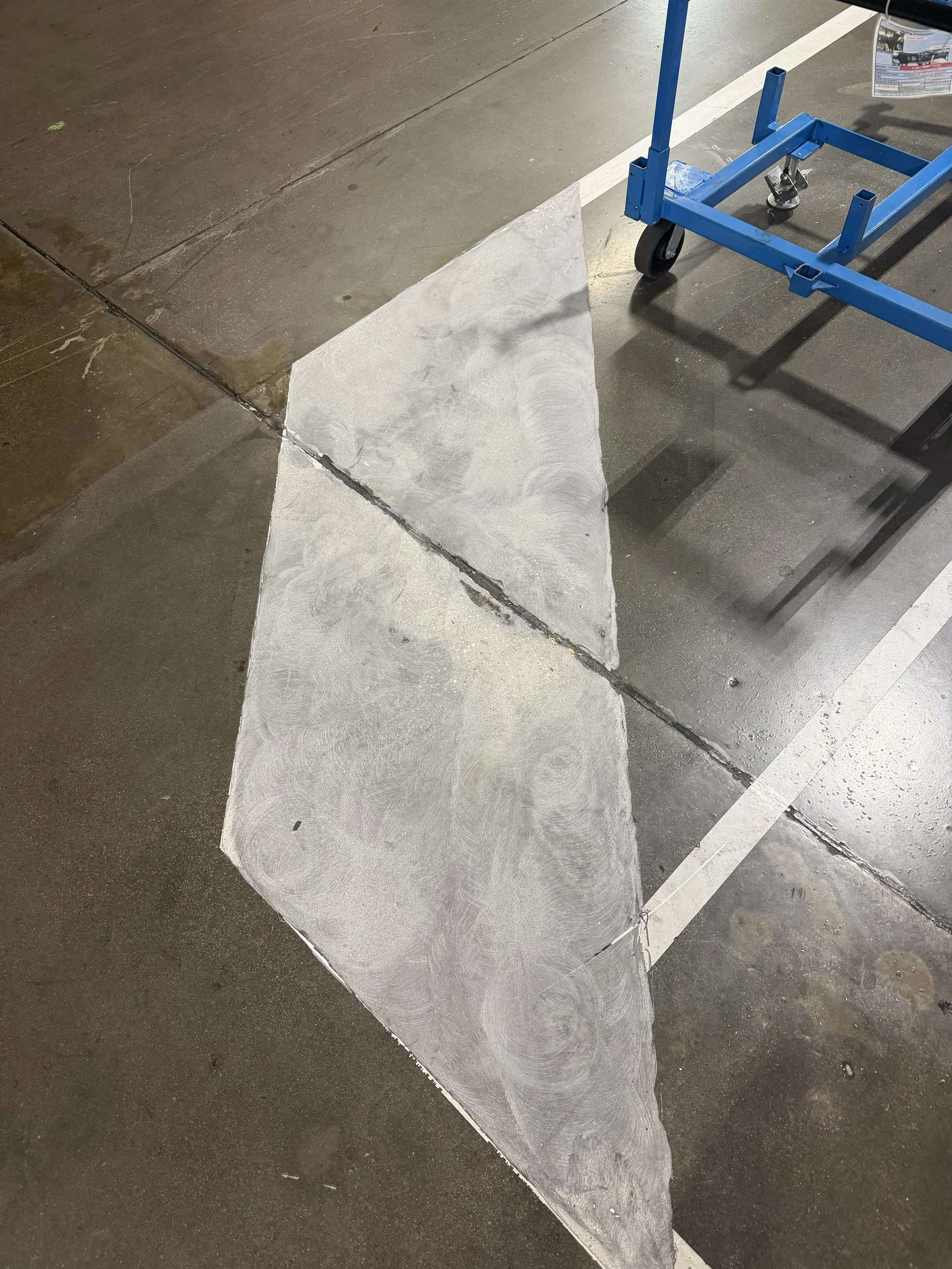 A close up of a factory floor with a section of freshly poured epoxy and a blue cart