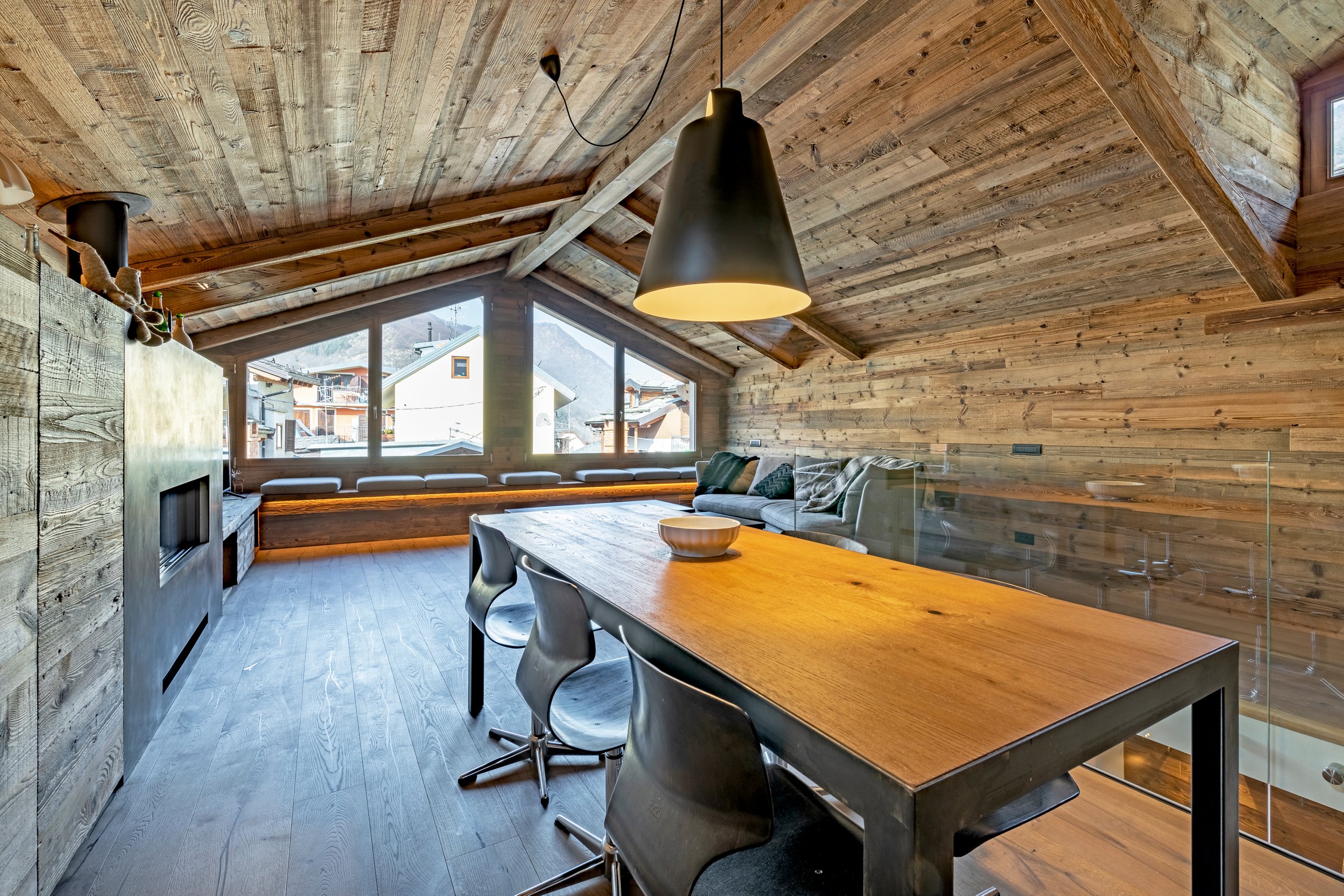 Interior of a modern wooden A-frame cabin with large windows, a chandelier, a dining table, and a cozy couch.