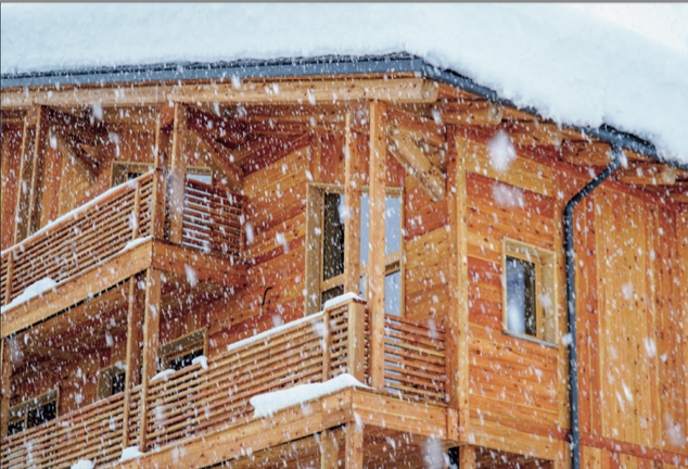 Wooden house covered in snow with snow falling.