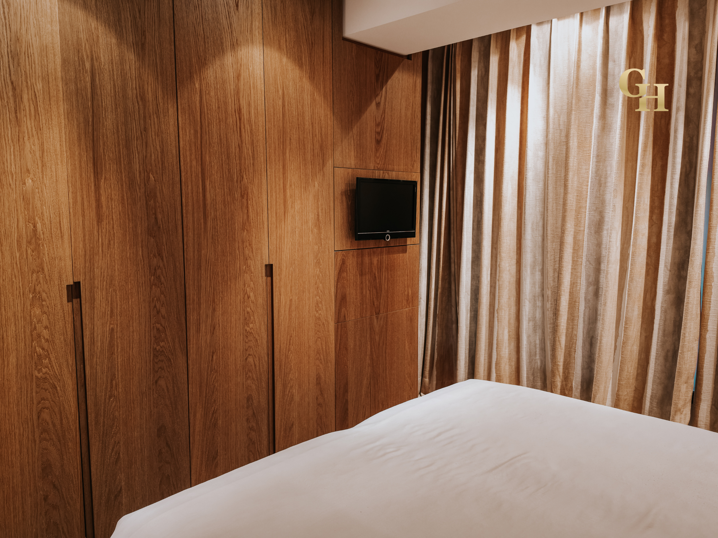 Hotel room with wooden wall panels, a window with curtains, and a small television.