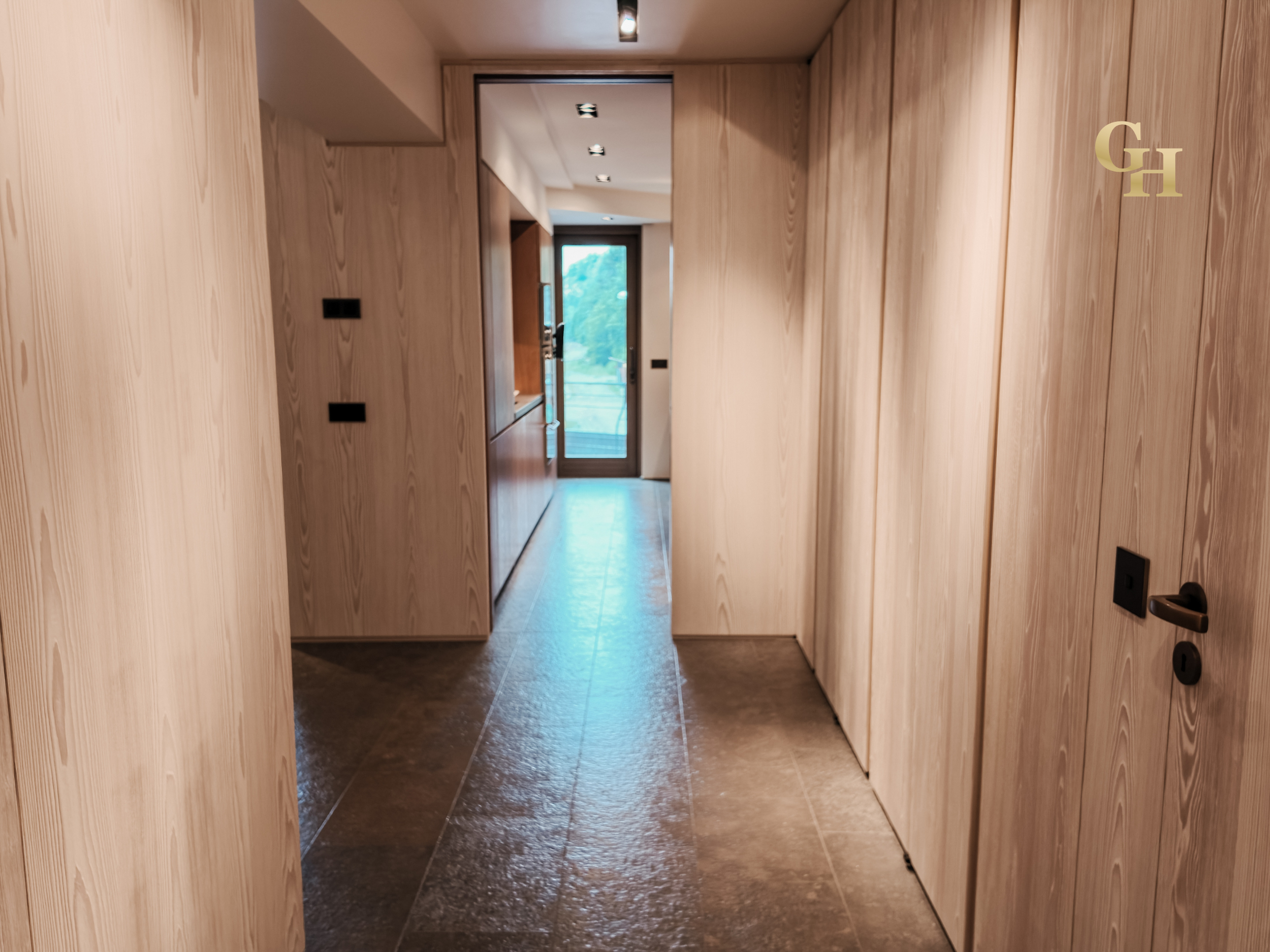 View of a hallway with wooden walls and floor, leading to a door with glass window showing an outdoor scene with trees.