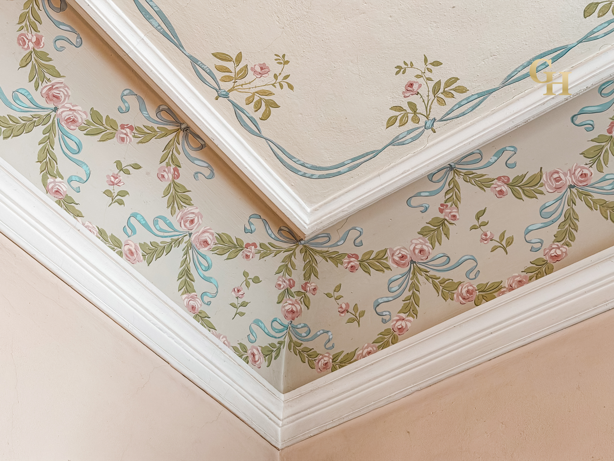 Decorative corner of a ceiling painted with floral and ribbon patterns in pink, green, blue, and beige colors.