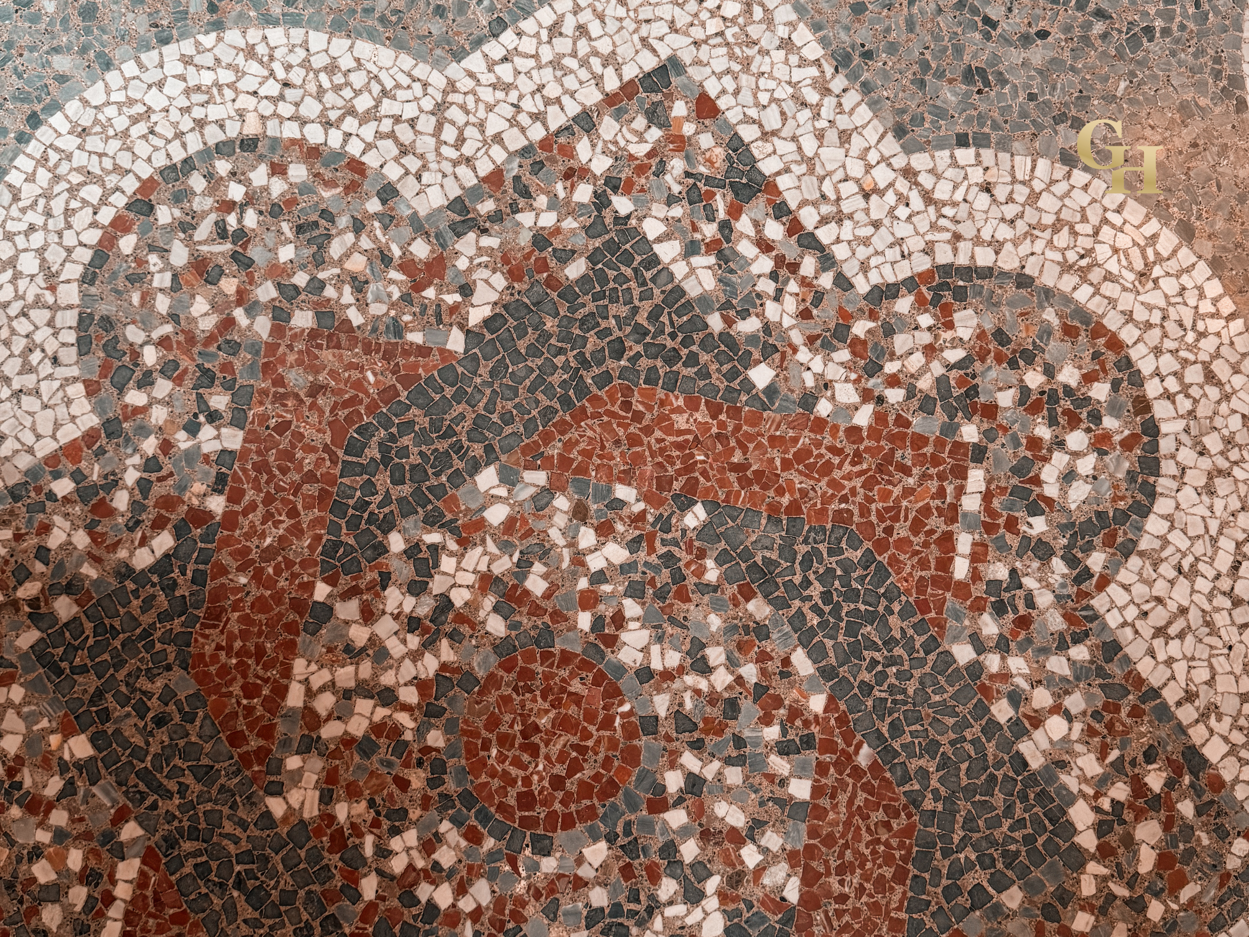 Close-up view of a decorative mosaic floor with a red, black, gray, and white pattern.