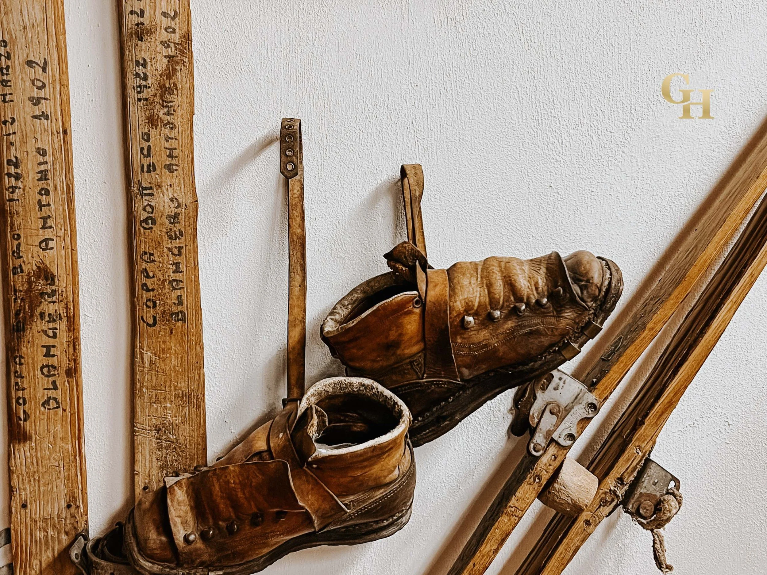 Collection of vintage leather boots, wooden planks with stamped numbers, and metal tools mounted on a white wall. Objects of the ski museum in Limone Piemonte, Piedmont, Italy.