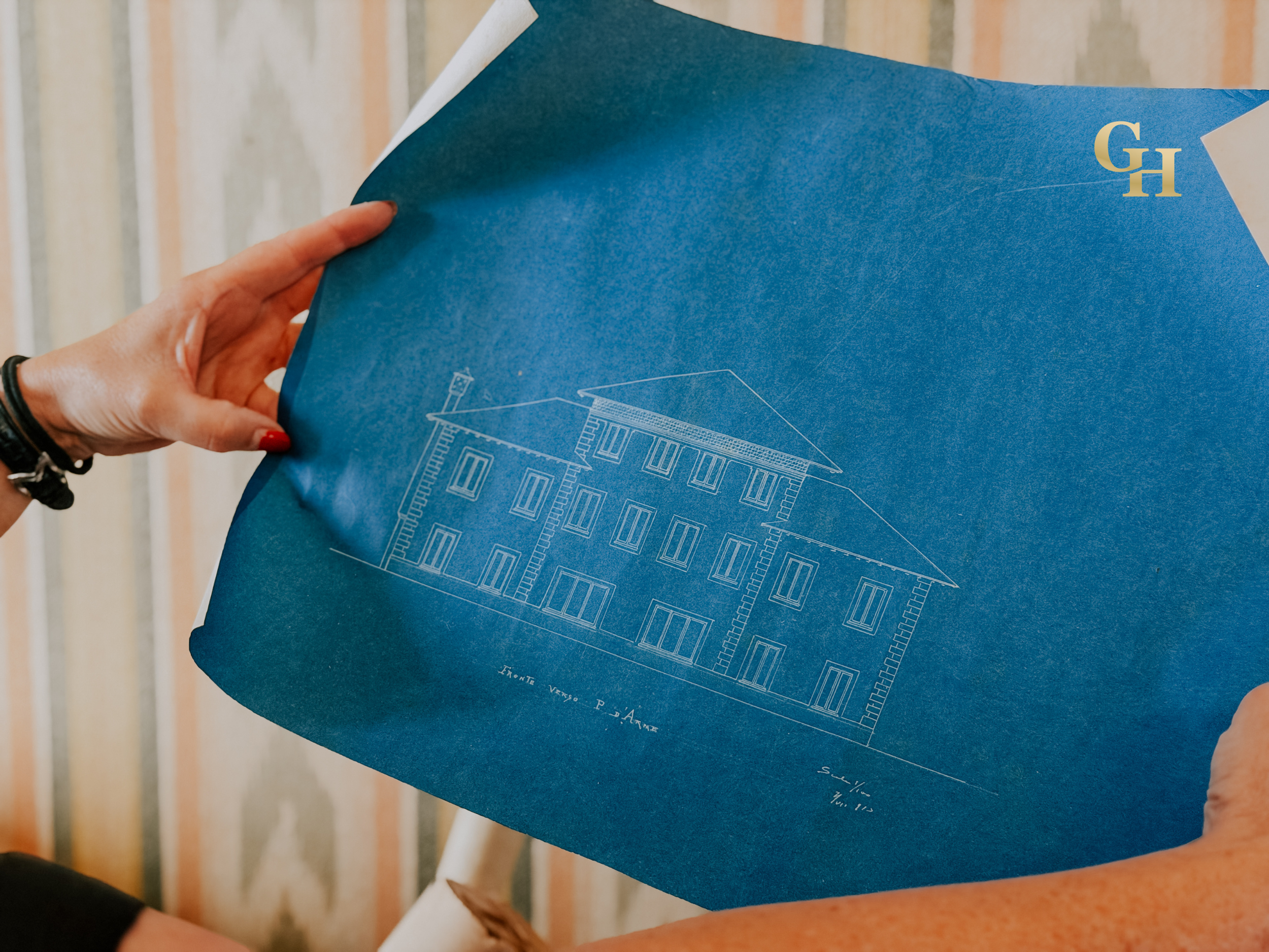A person holding a blue blueprint of a building, with white architectural drawings and text on it.