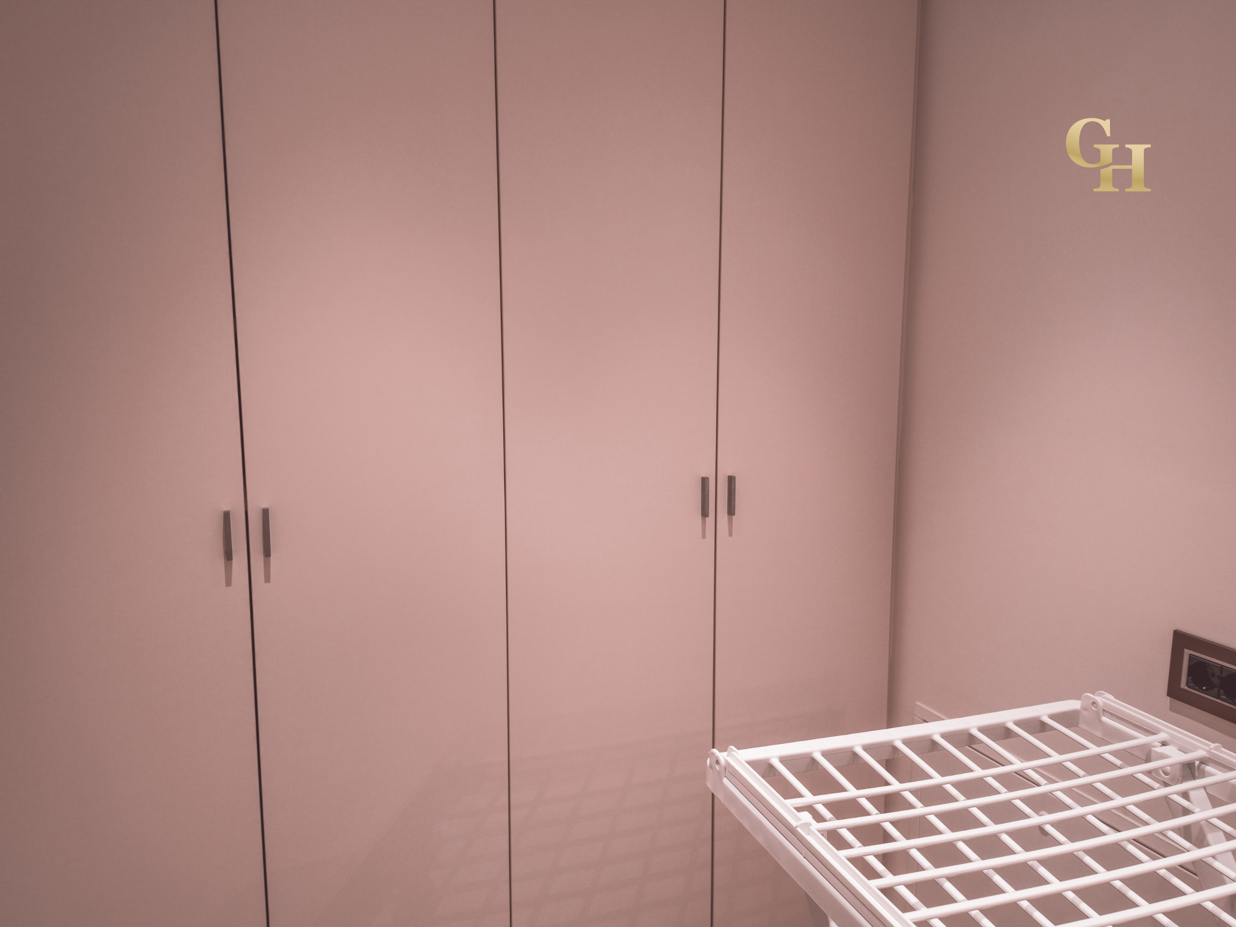 Pink closet with closed doors and silver handles. Part of a white drying rack in the foreground and a wall outlet in the lower right corner.