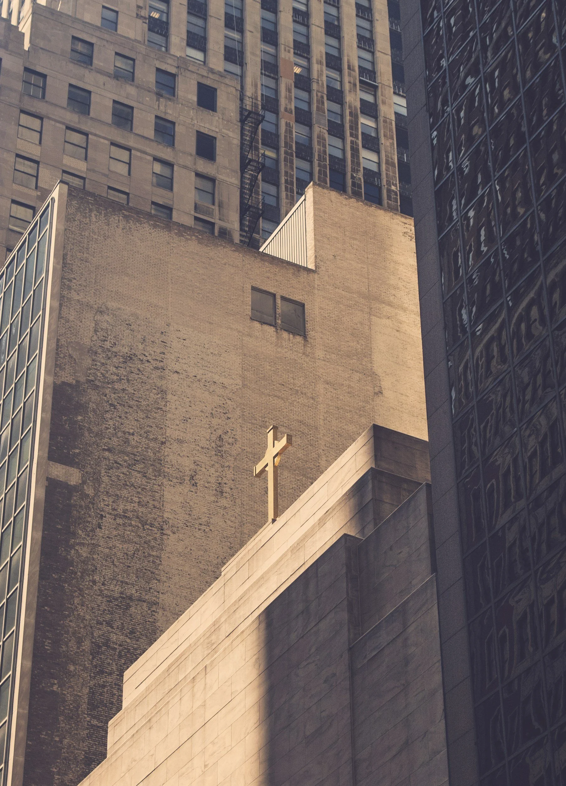 A cityscape of tall buildings, including a church with a cross on top, seen from below, with modern glass and older stone architecture.