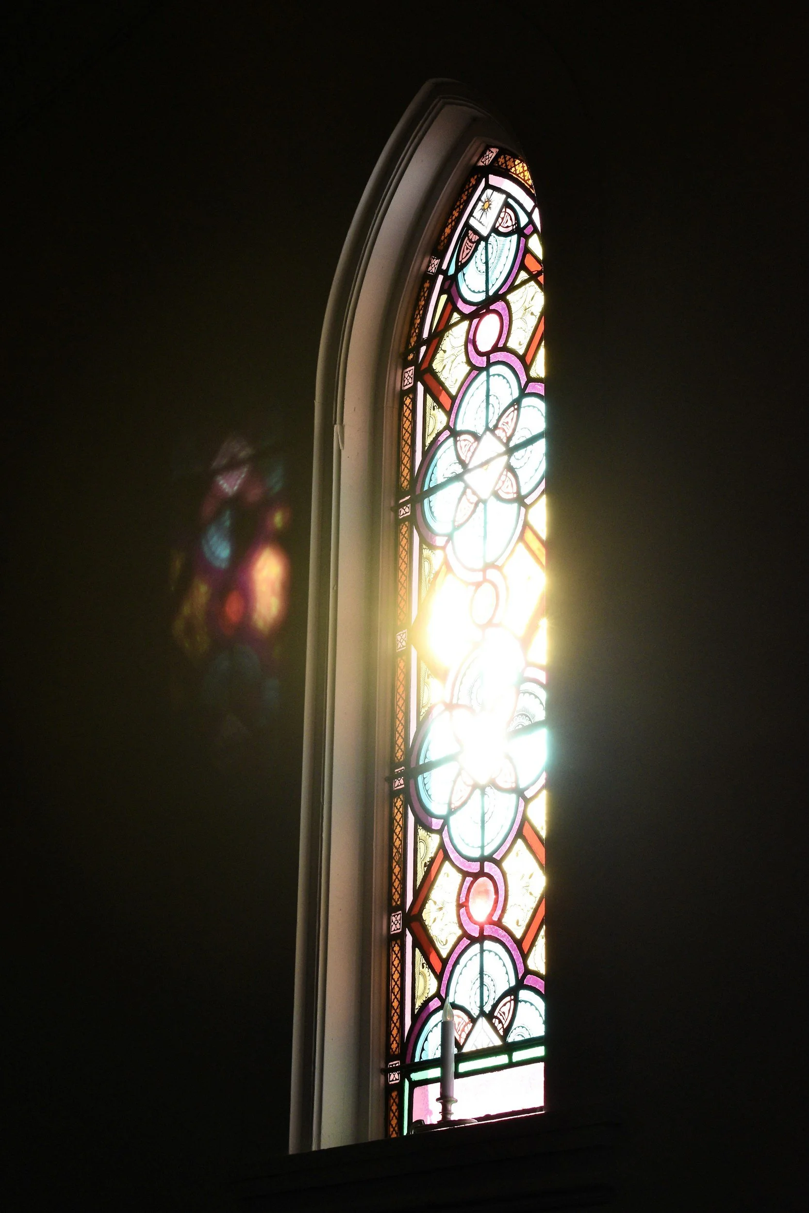 Colorful stained glass window with floral and abstract designs, sunlight streaming through and casting reflections.