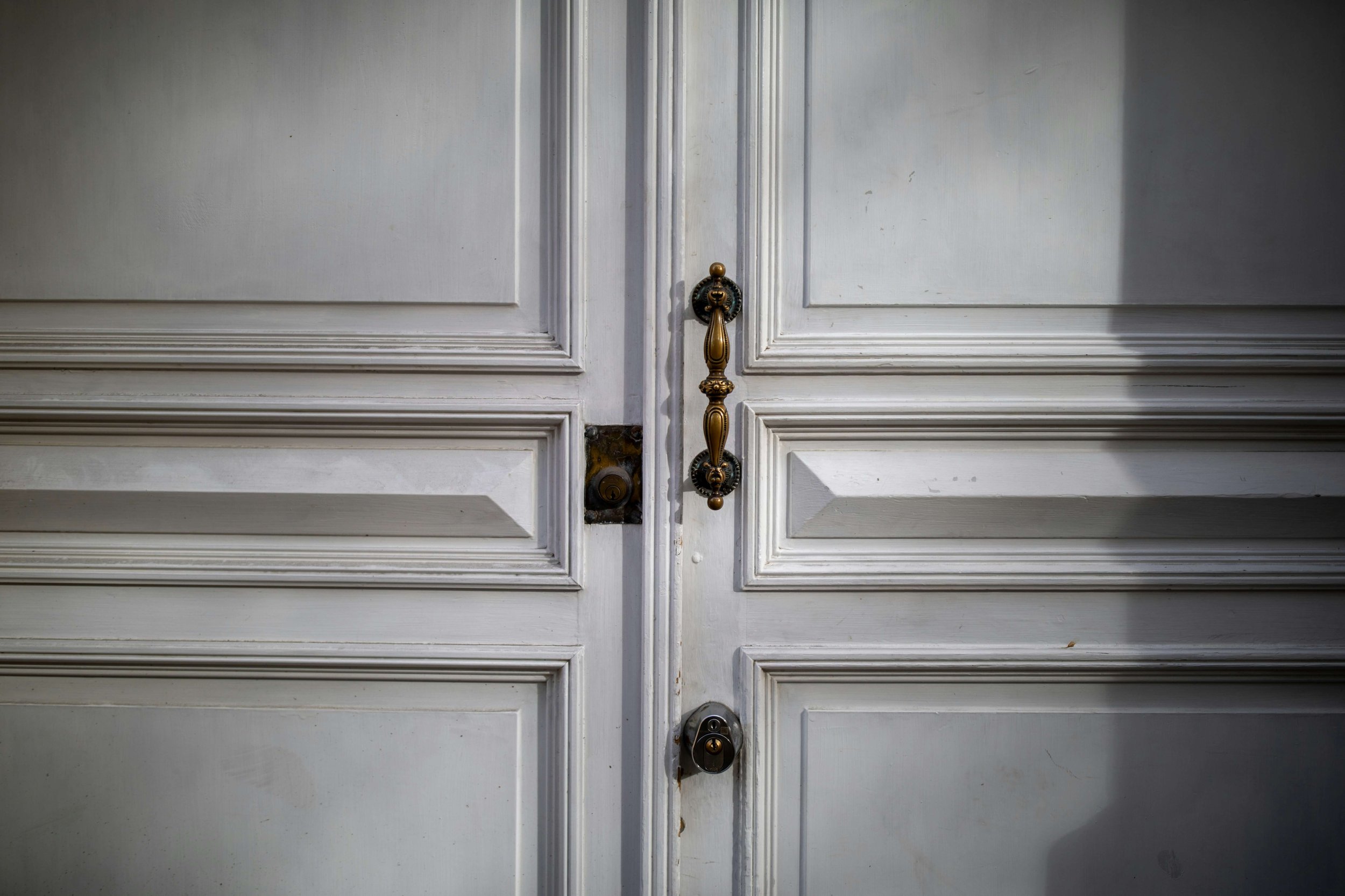 Close-up of ornate brass hardware and locks on a white paneled double door