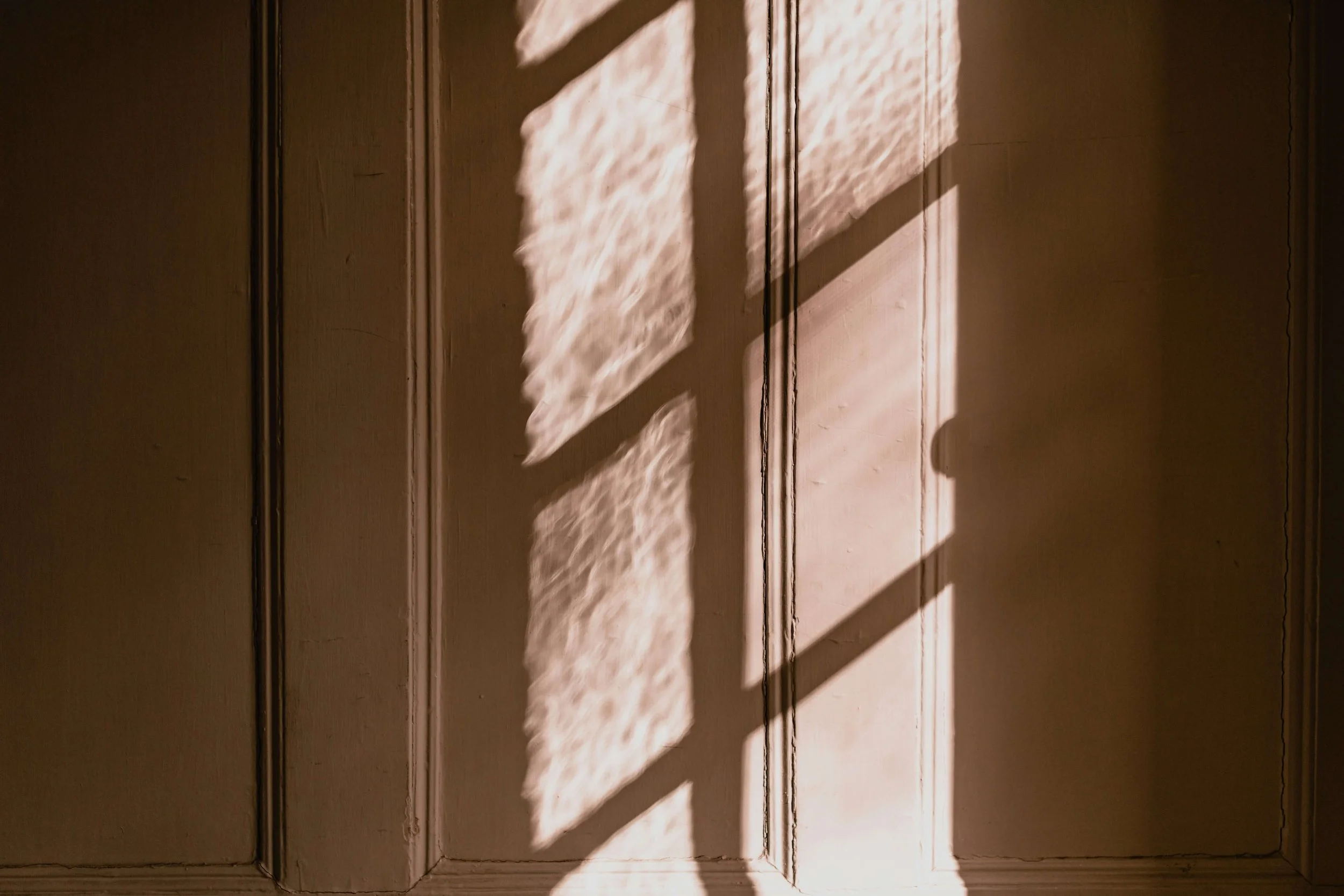 Warm sunlight and window-blind shadows cast across a wooden paneled wall