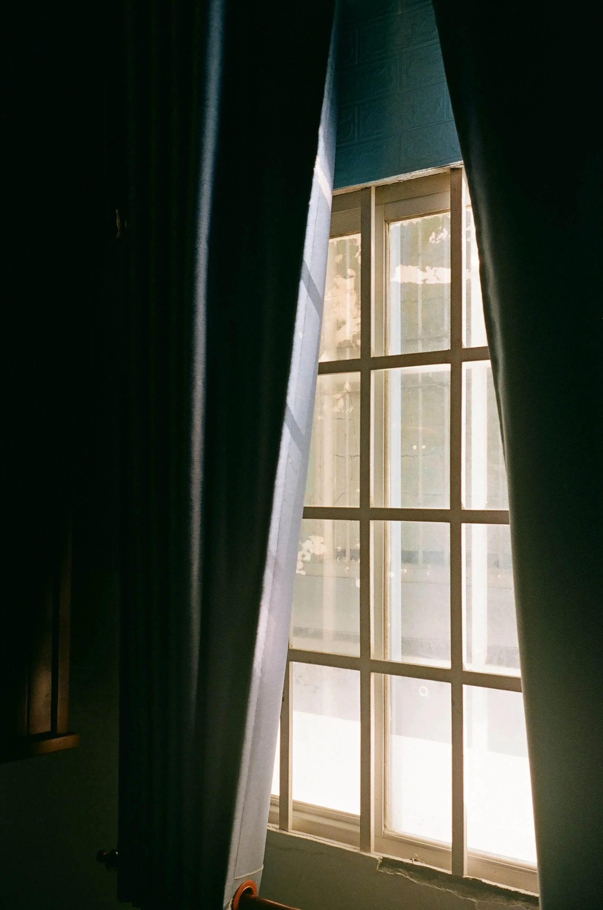 Sunlight streaming through a multi-pane window framed by dark curtains and a sheer white curtain.