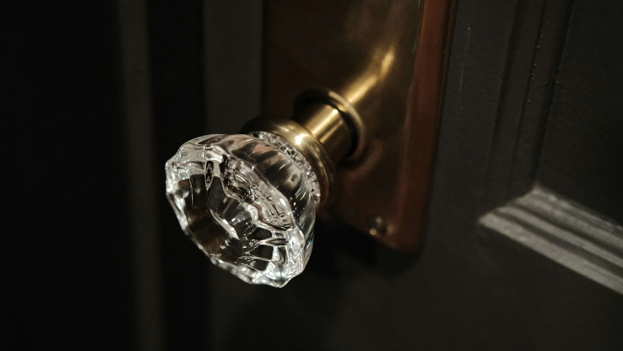 Close-up of a faceted crystal glass door knob with a brass mounting plate on a dark wooden door