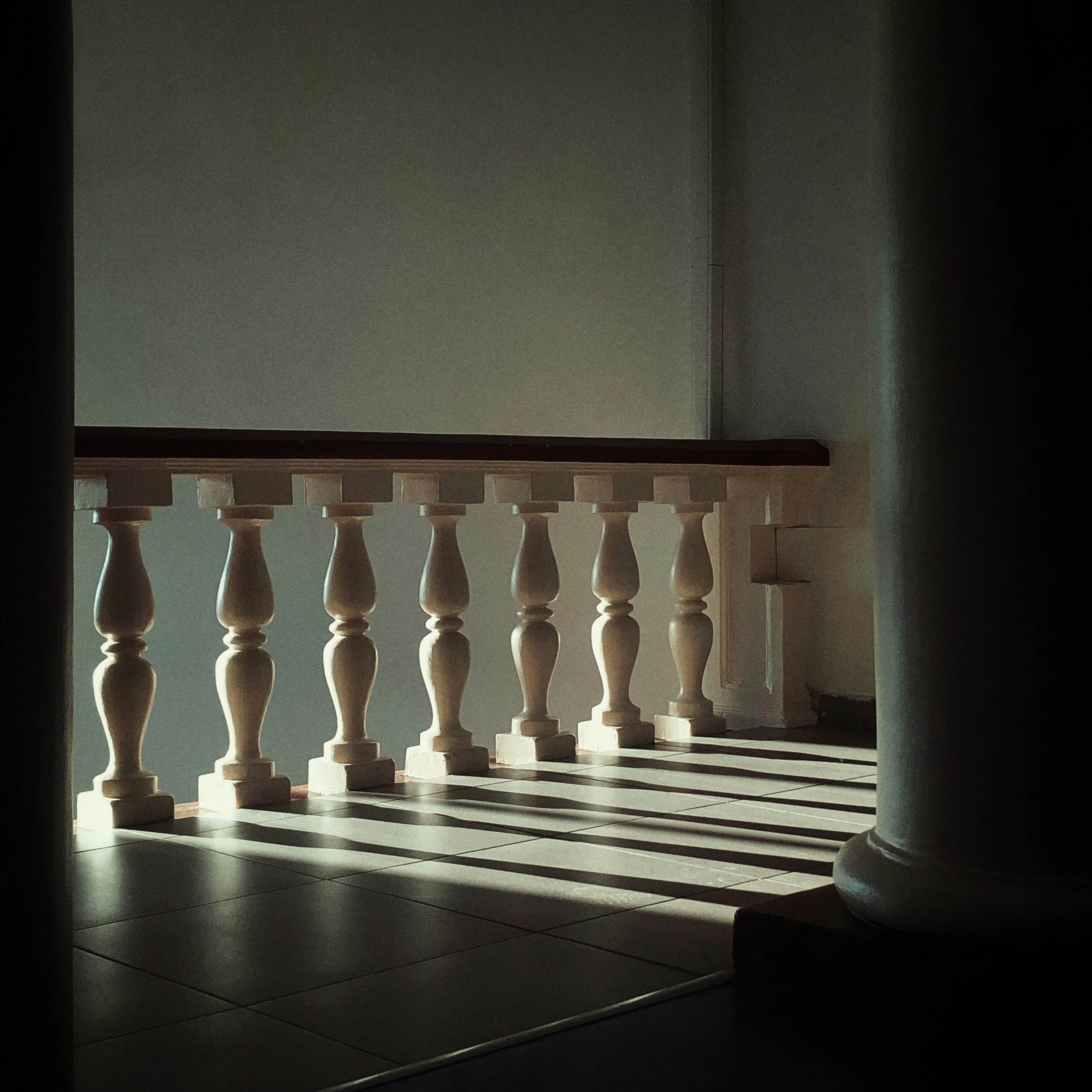 Sunlit white balustrade with turned spindles and tiled floor in a shadowy interior