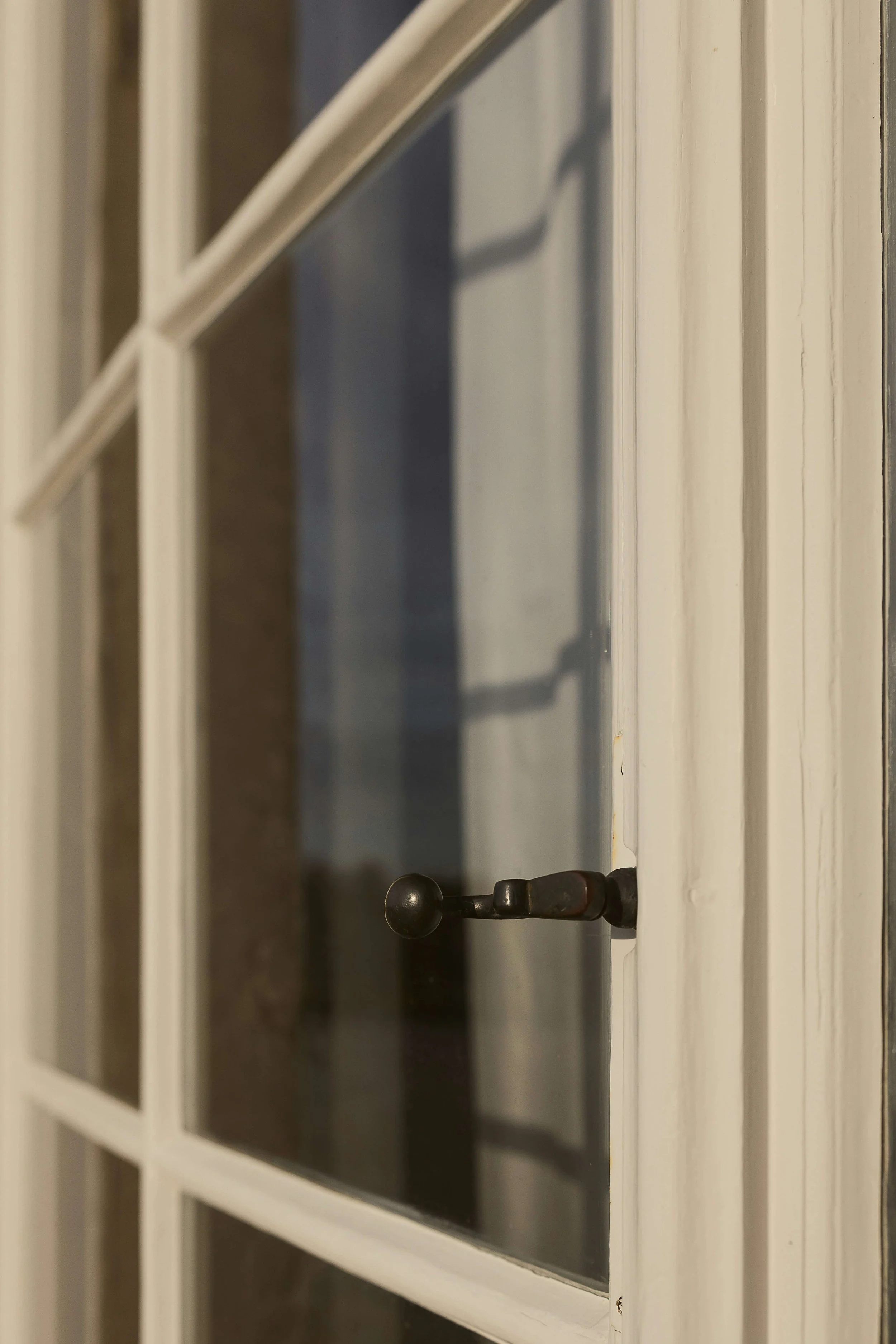 Close-up of an open white-framed window with a black metal latch and diagonal muntins.