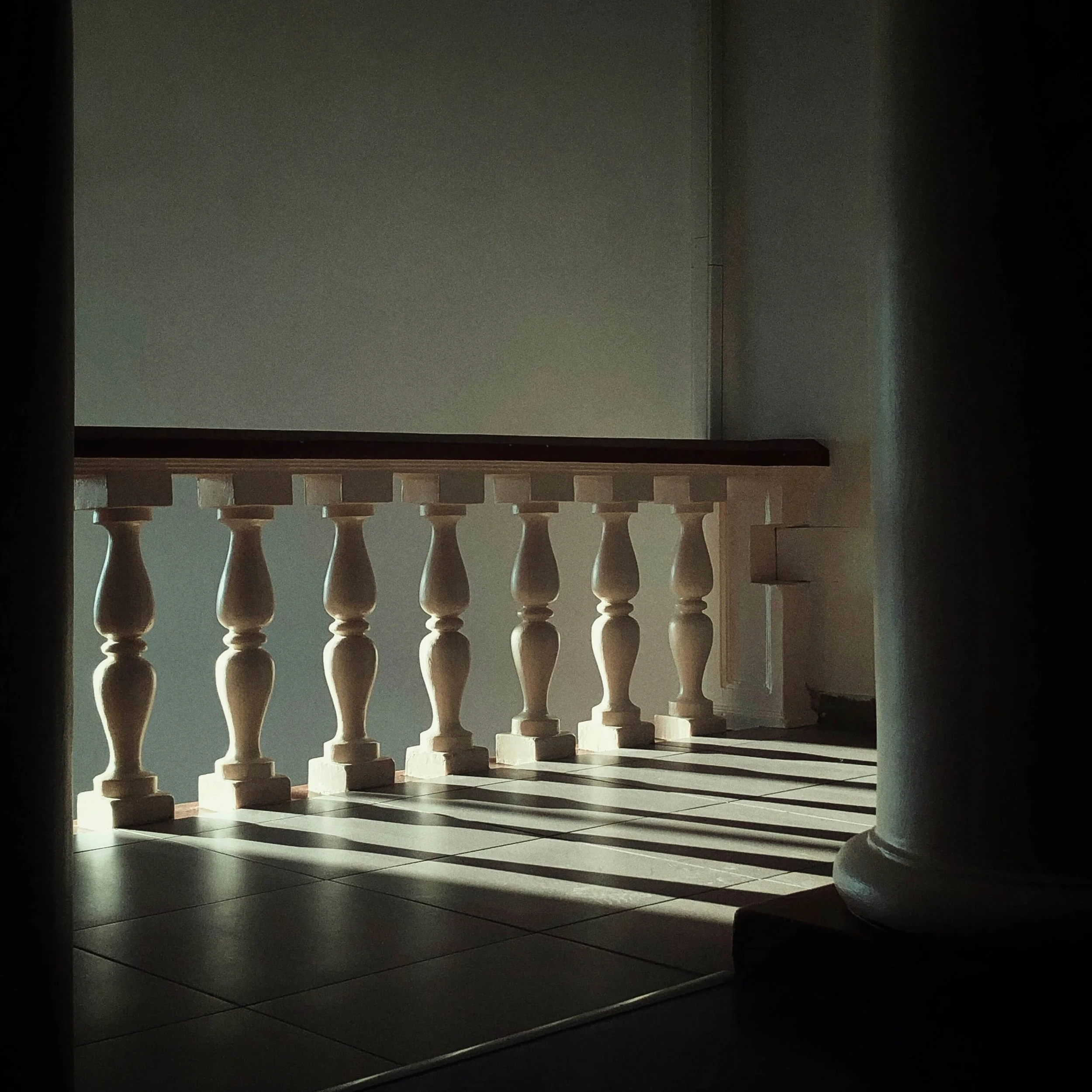 Sunlit cream-colored wooden balustrade along a tiled balcony with dramatic shadows