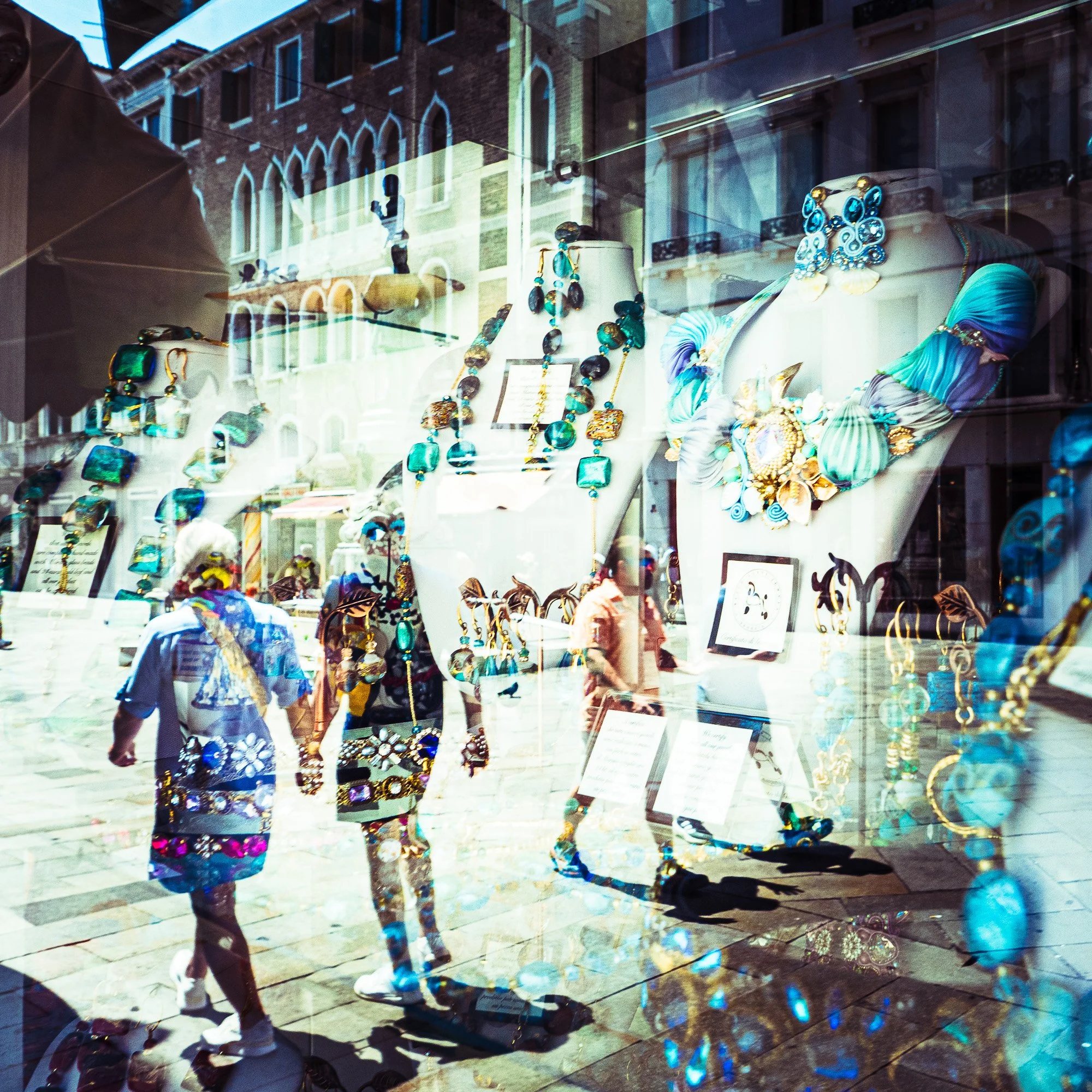 Schaufenster mit Schmuck und Accessoires, Reflektionen von Gebäuden und Menschen auf der Glasscheibe.