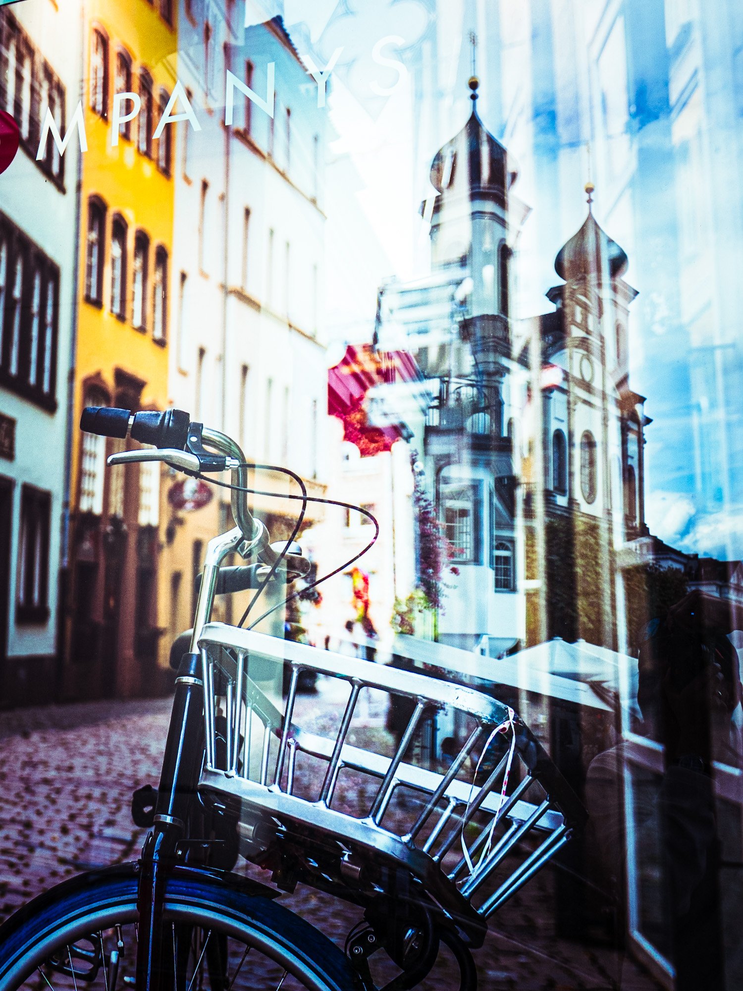 Fahrrad im Schaufenster mit reflektierenden Gebäuden und Kirchtürmen im Hintergrund.