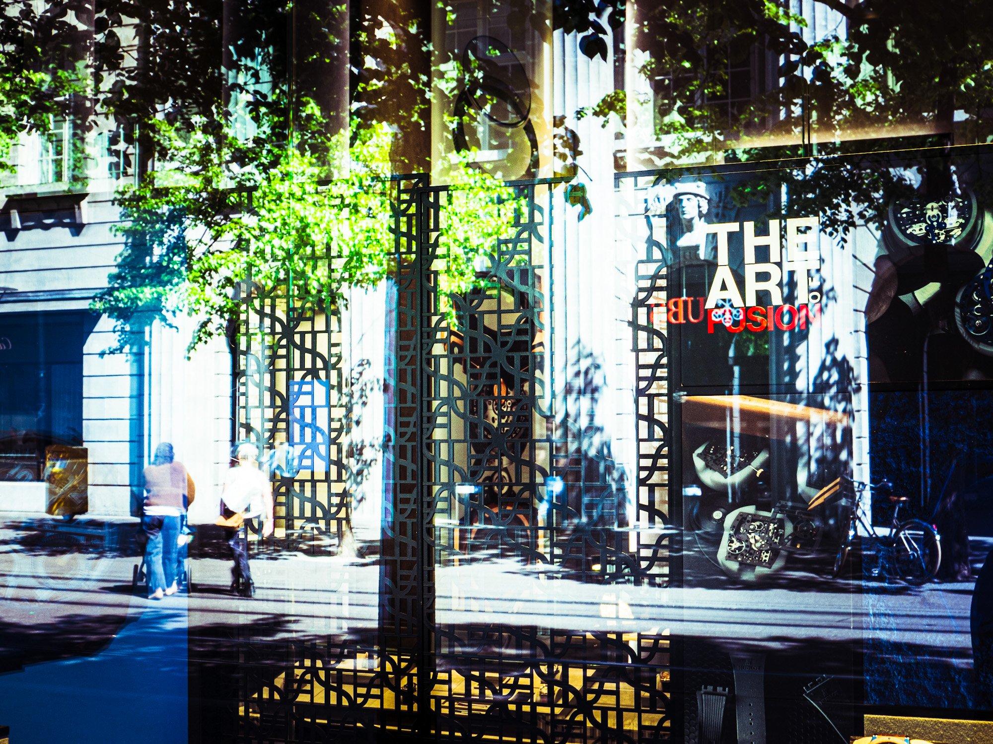 Schaufenster eines Kunstmuseums mit stilisiertem Kunstwerk, Schriftzug 'The Art of Fusion', reflektierende Oberflächen, grüne Bäume im Hintergrund, Vitrinen mit Kunstwerken, Menschen vor dem Fenster.