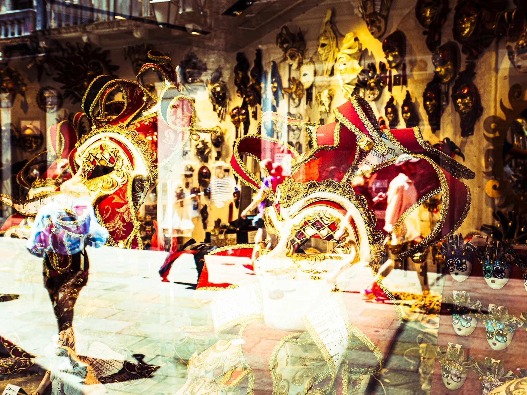 Verkauf von venezianischen Masken und Kronen in einem Schaufenster, mit Masken an der Wand im Hintergrund.