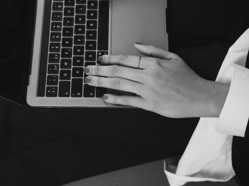 A person typing on a laptop keyboard with their right hand, wearing a white shirt and a dark blazer.
