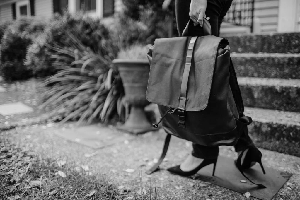 A person carrying a large backpack while walking up outdoor stone stairs, wearing high-heeled shoes.