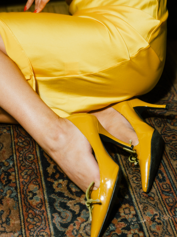 Close-up of a person wearing yellow high heels and a yellow dress, sitting on a patterned carpet.