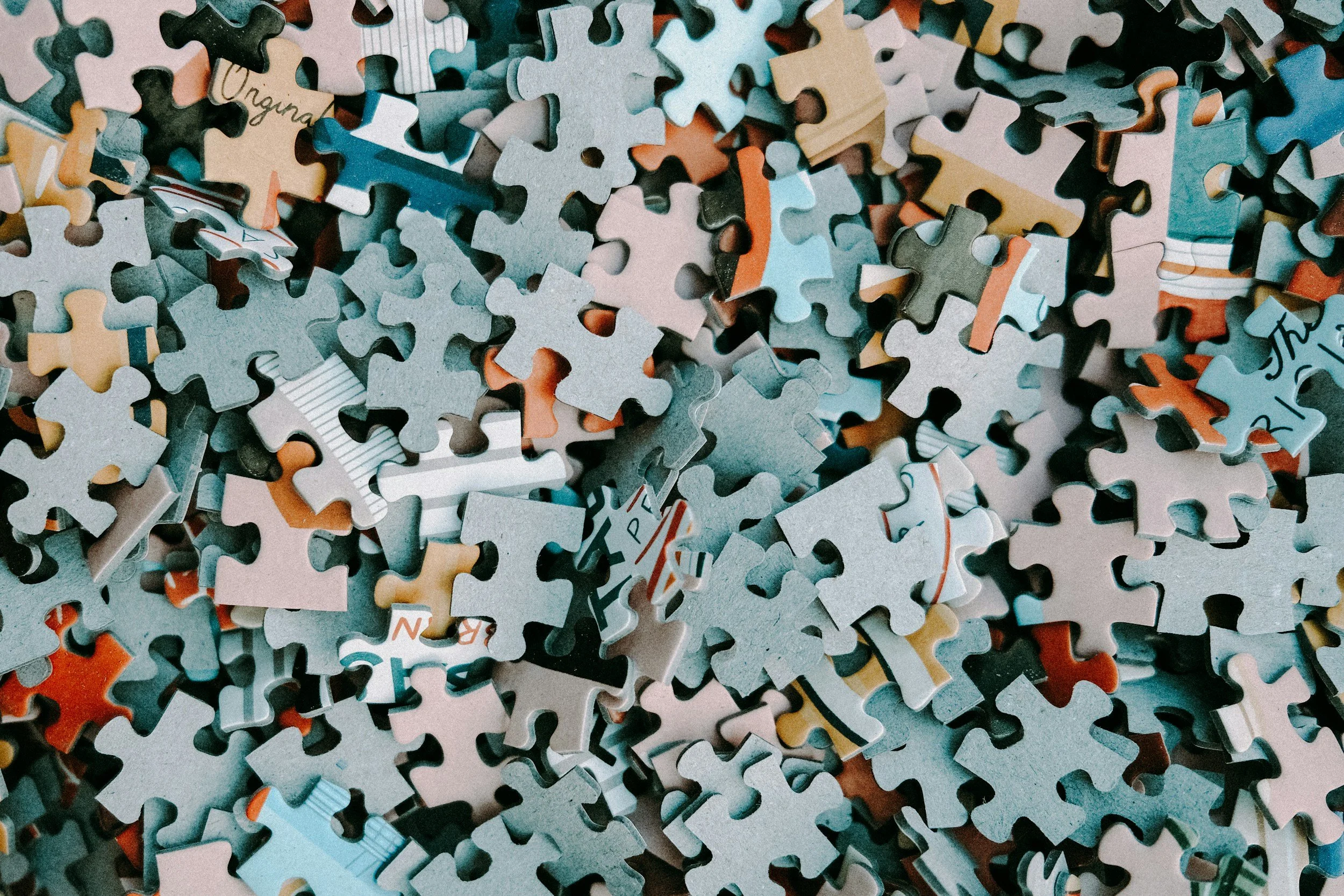 A close-up image of scattered jigsaw puzzle pieces in various colors and patterns, mostly face down, with some showing partial text or images.
