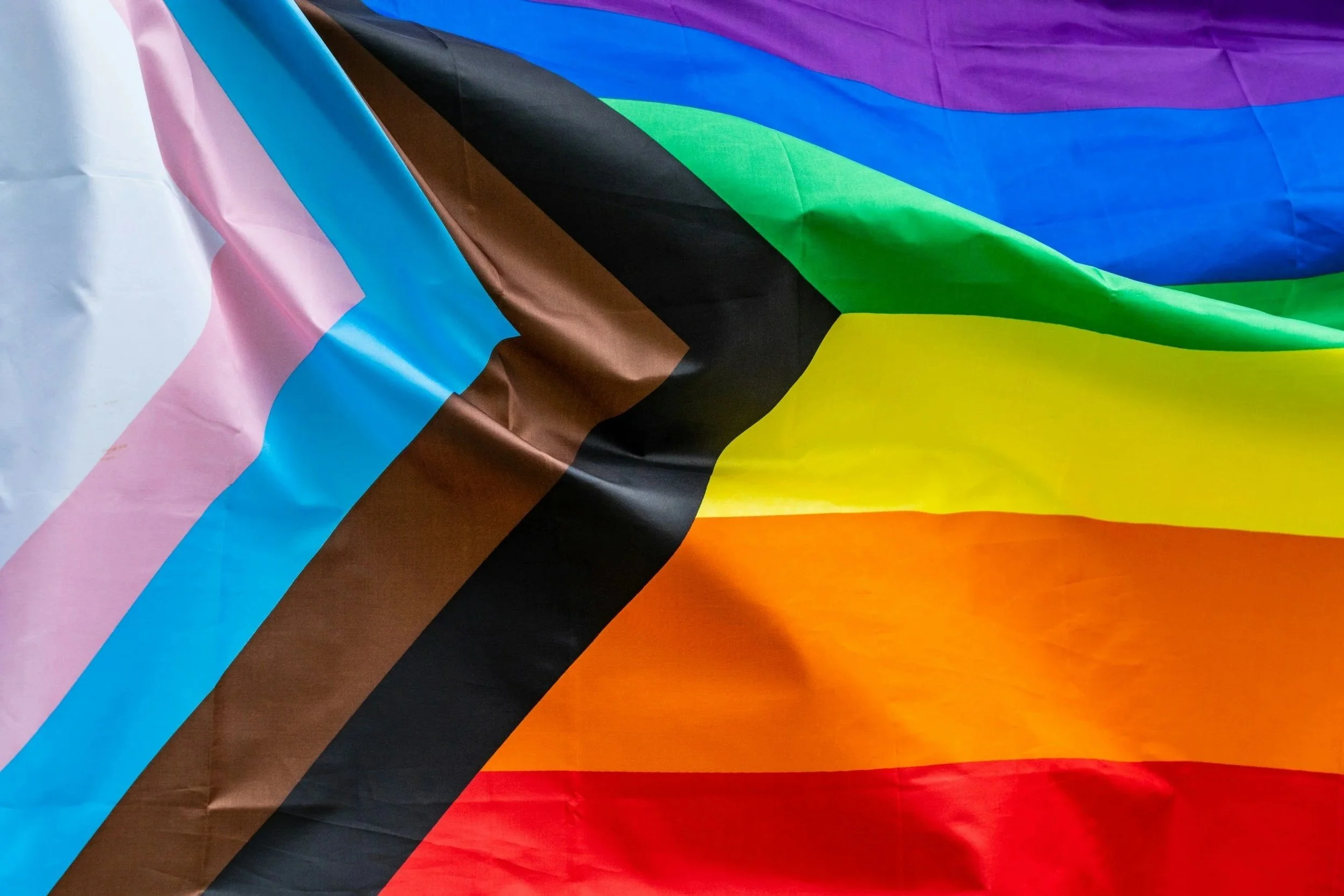 Close-up image of a multicolored pride flag with horizontal stripes in various colors including purple, blue, green, yellow, orange, red, and black.