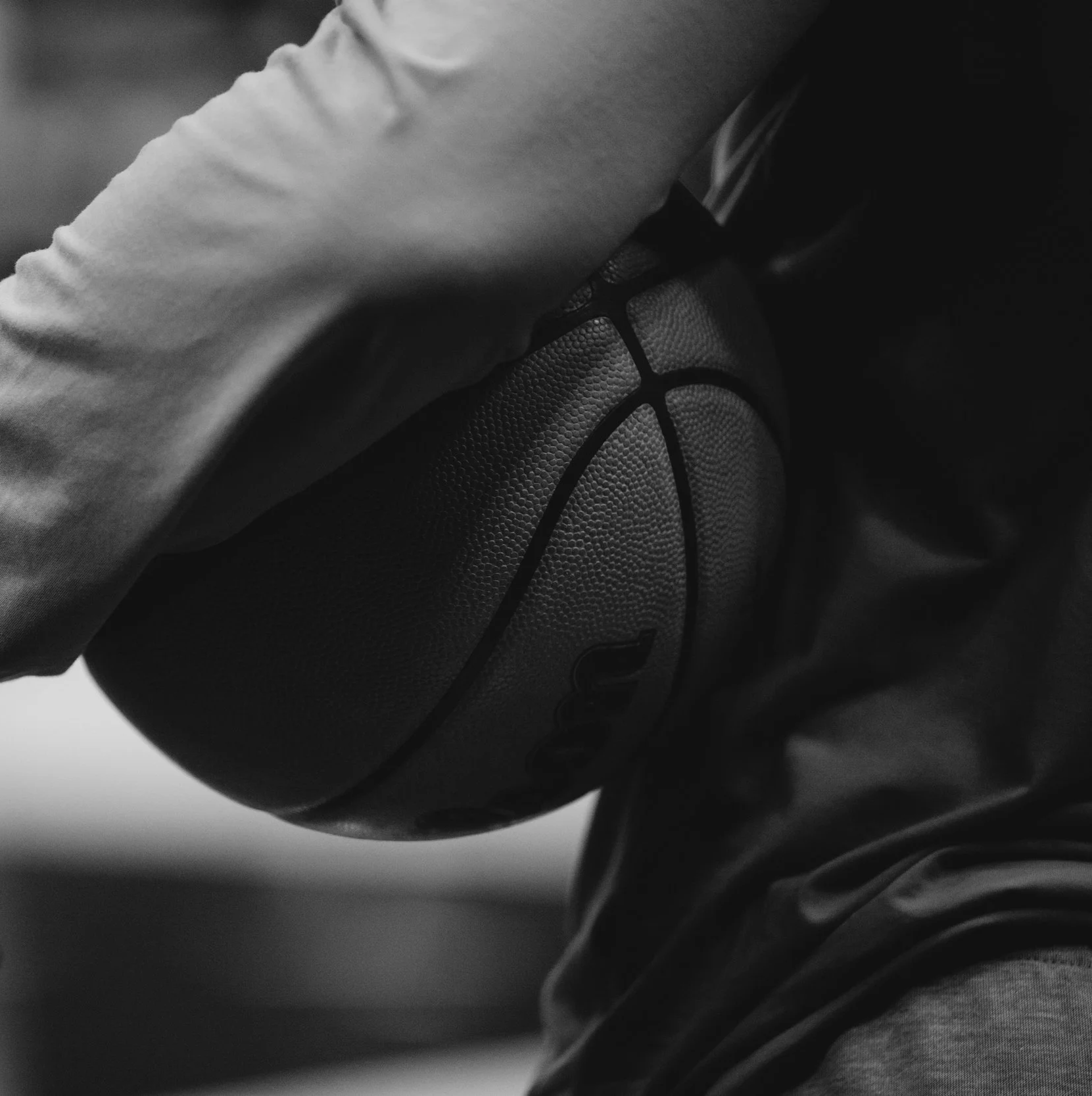 Close-up black and white photo of a person’s hand resting on a textured basketball, with the person's sleeve partially covering the hand.