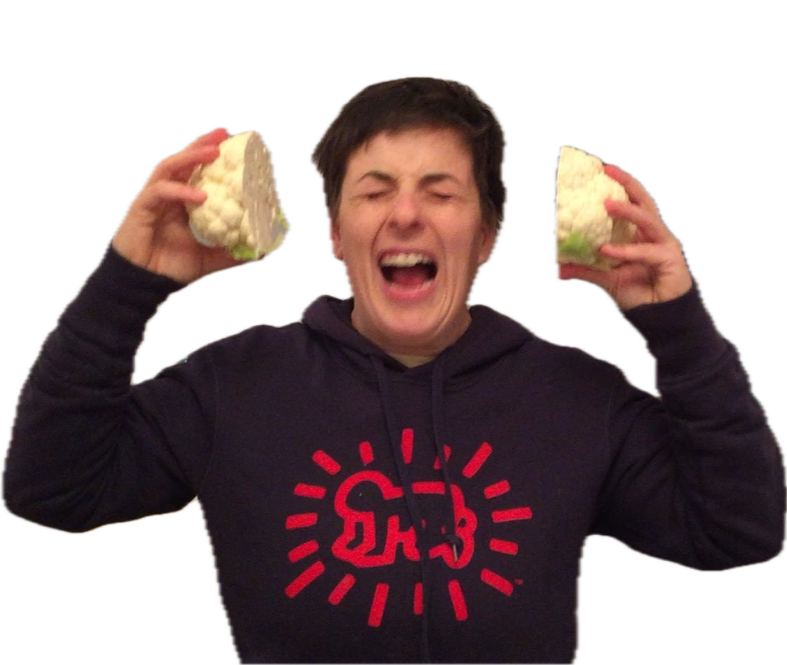 Winter Miller wearing a black hoodie with a red graphic holding two large pieces of cauliflower, one in each hand, and smiling with eyes closed.