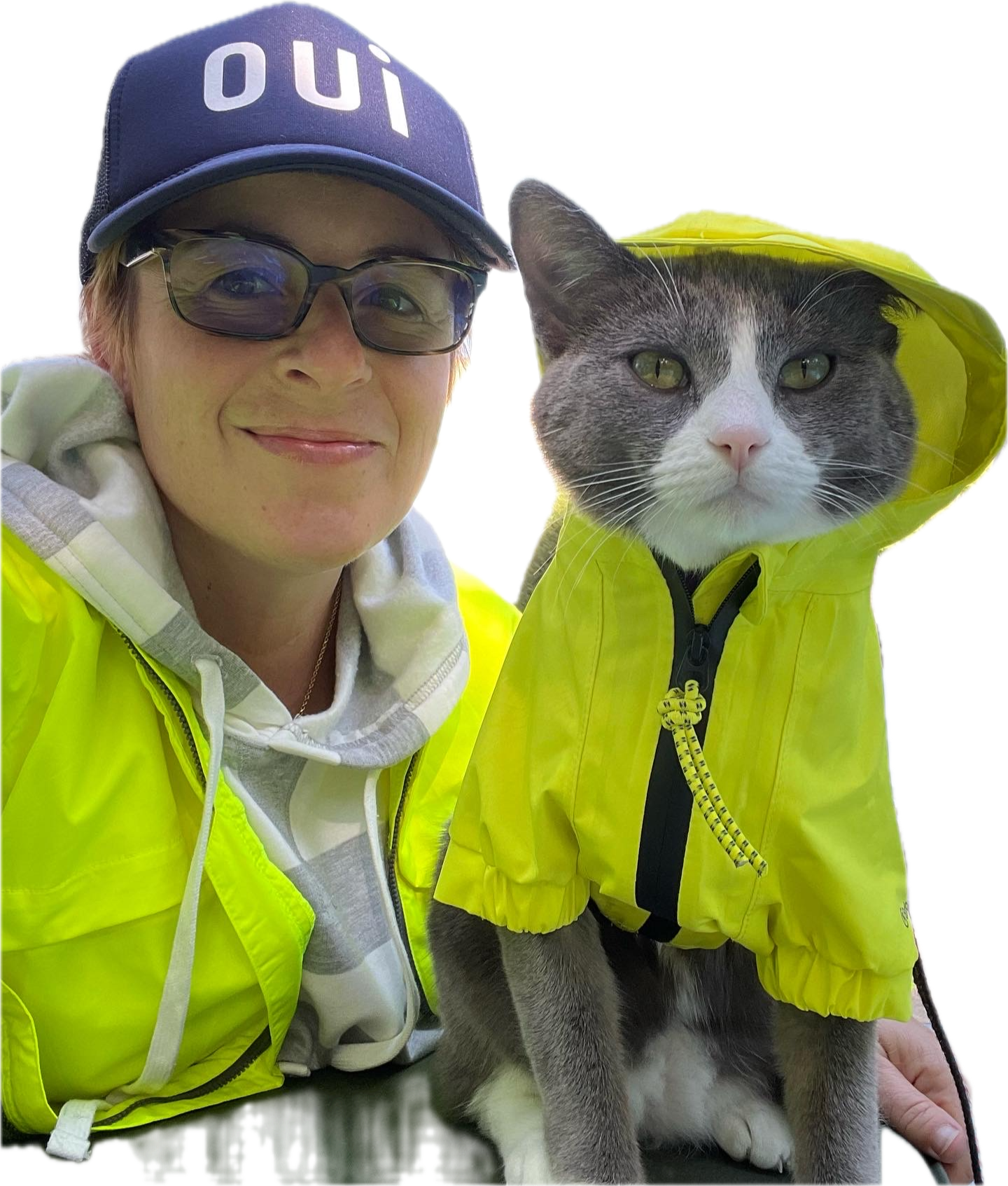 Winter Miller wearing glasses, a blue cap with the word 'oui' and a yellow jacket, poses with a gray and white cat wearing a matching yellow jacket with a hood and black zipper.