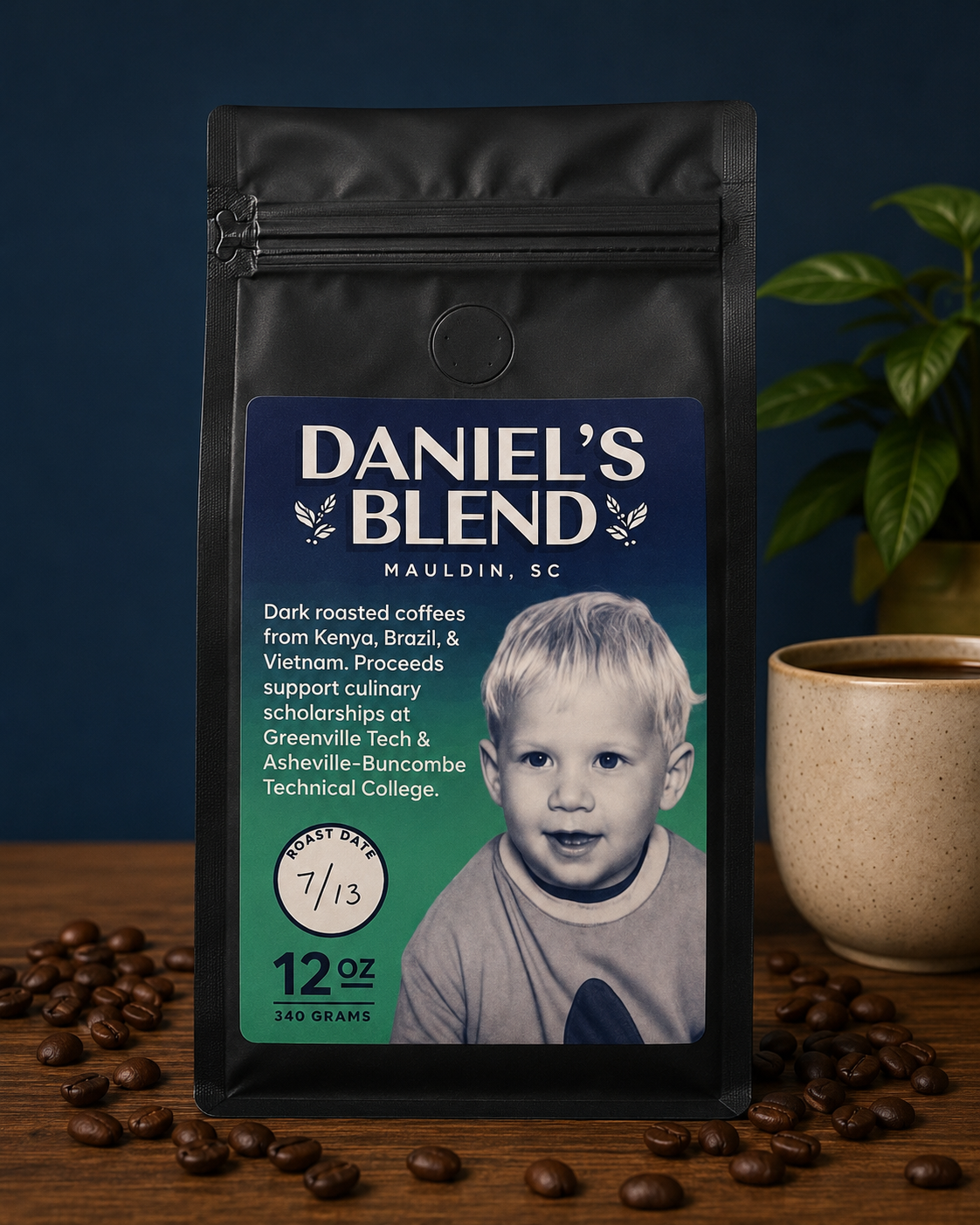 Package of Daniel's Blend dark roast coffee with a photo of a young boy on the label, placed on a wooden surface with scattered coffee beans, a beige mug of coffee, and a green potted plant beside it.