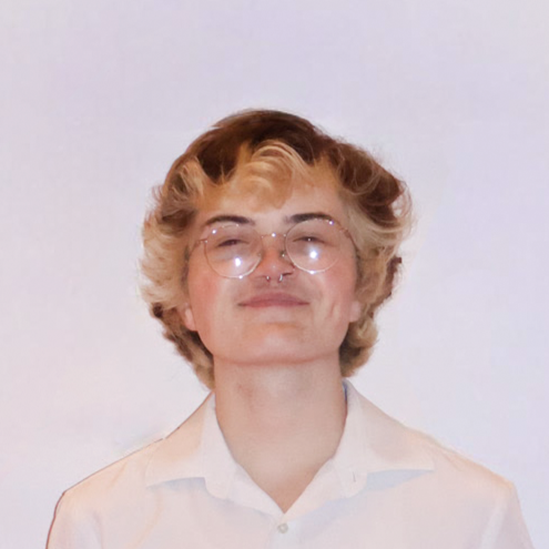 Person with curly blonde hair and glasses smiling against a plain white background.