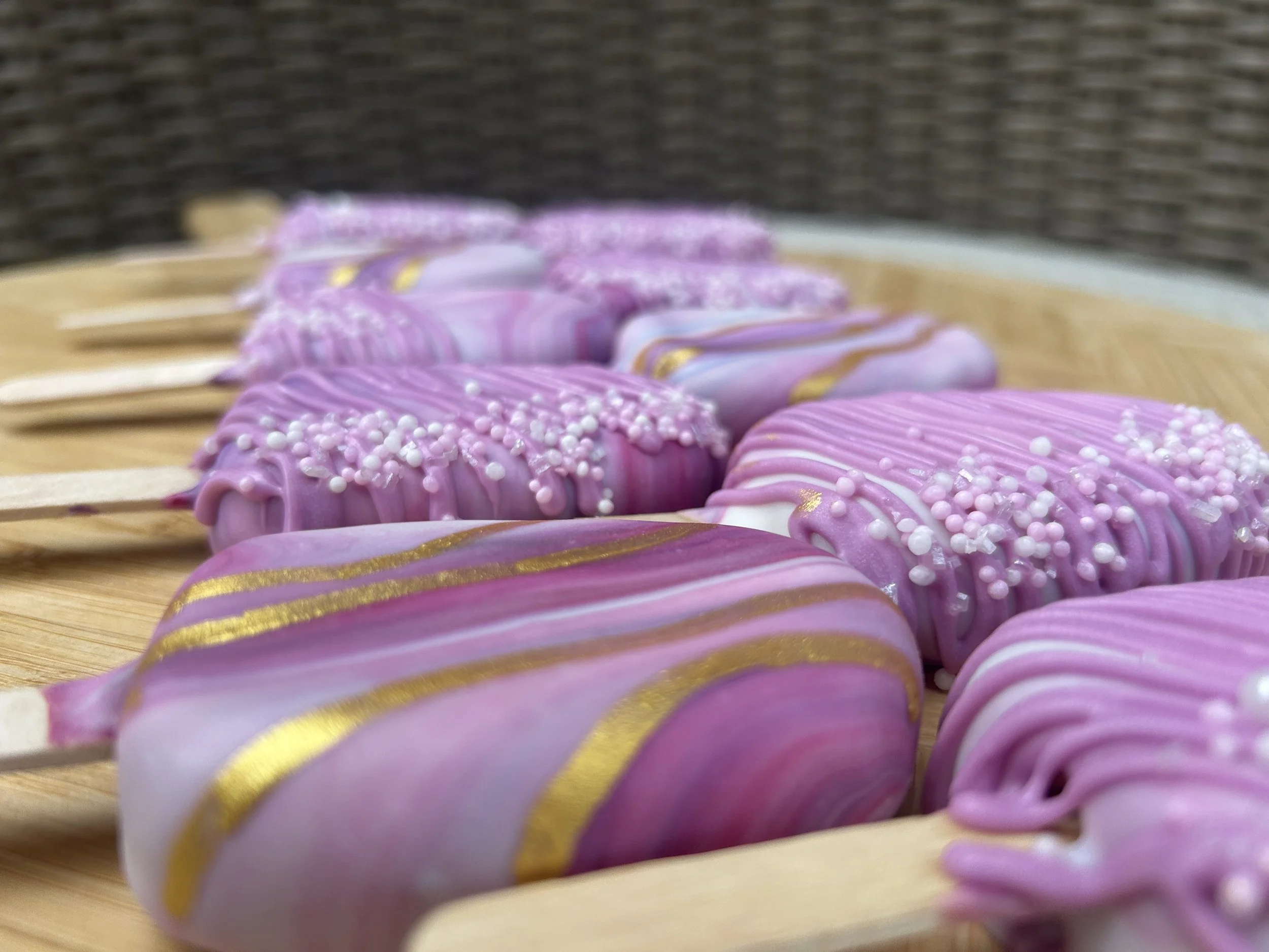 Close-up of decorated pink and white cookies with gold and white sprinkles, arranged on a wooden surface