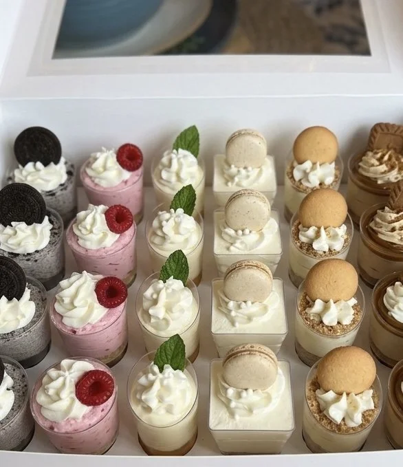 Assorted mini cheesecakes with various toppings, including Oreos, raspberries, mint leaves, macarons, and crumbled cookies.