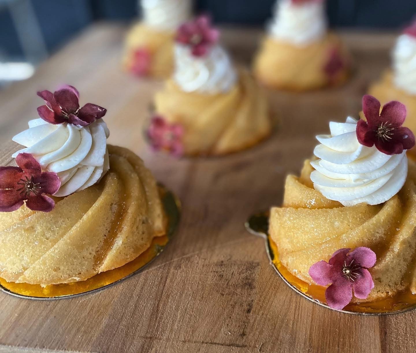 Close-up of decorative mini pumpkin desserts topped with white whipped cream and small purple flower decorations, set on a wooden surface.