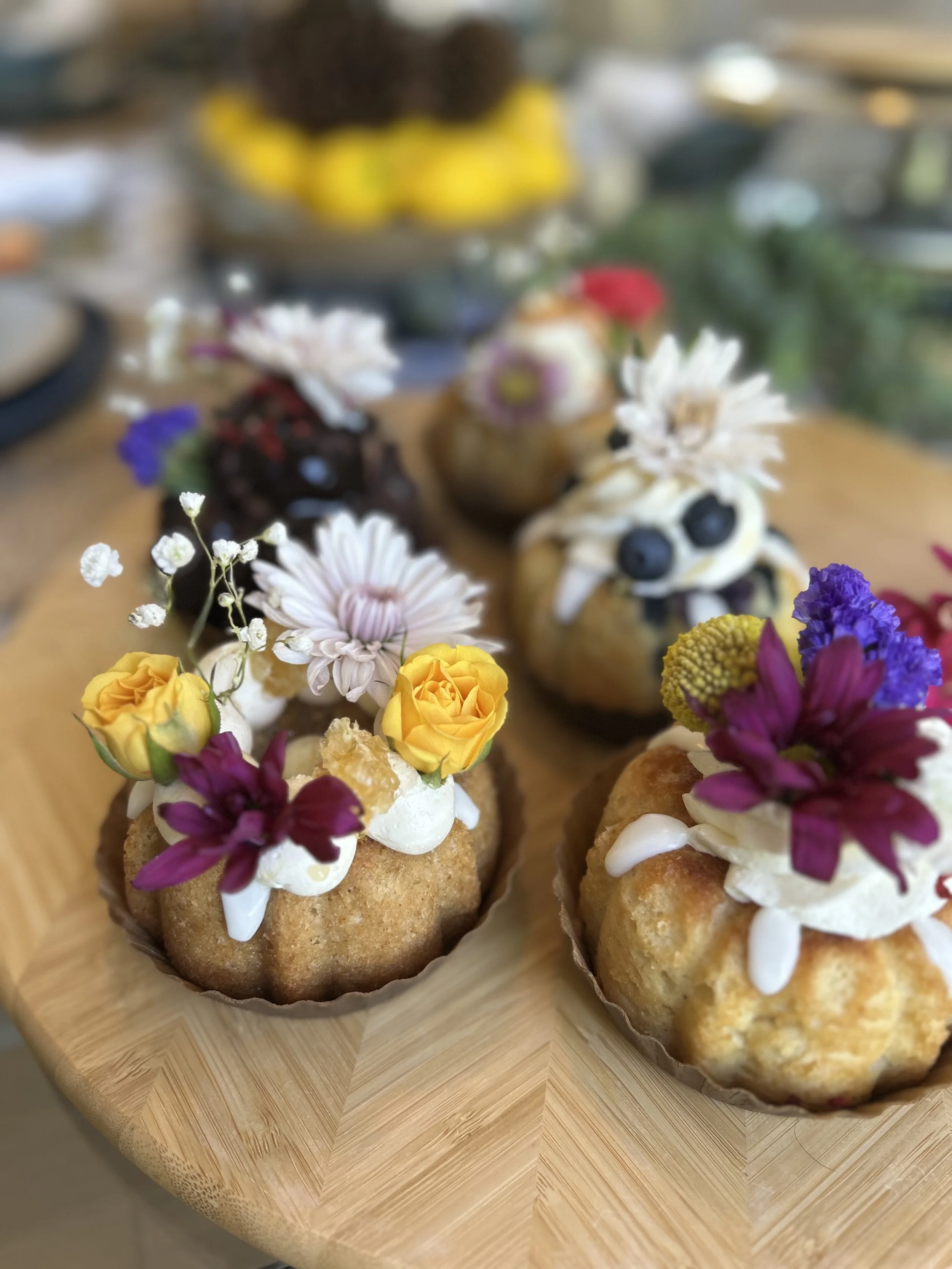 Close-up of three decorated cupcakes with flowers on top, placed on a wooden tray.