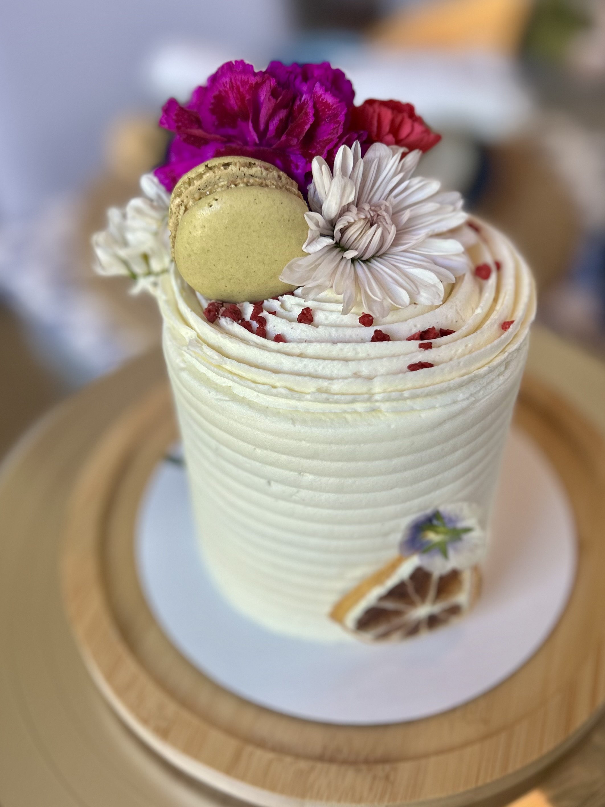 Close-up of a cake decorated with flowers, macarons, and sprinkles, viewed through a circular object.