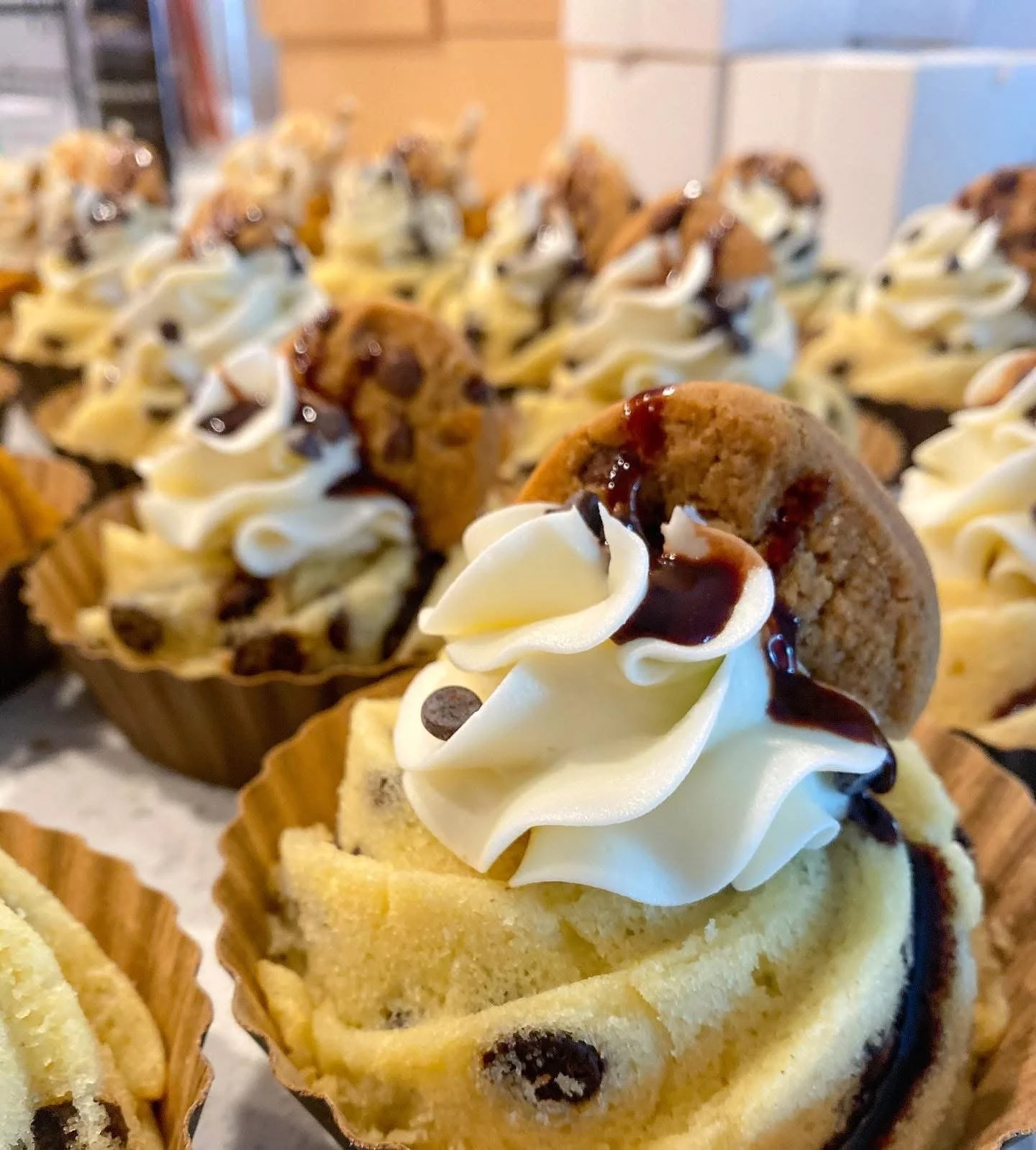 Close-up of decorated cupcakes with vanilla frosting, chocolate chips, chocolate drizzle, and a cookie on top