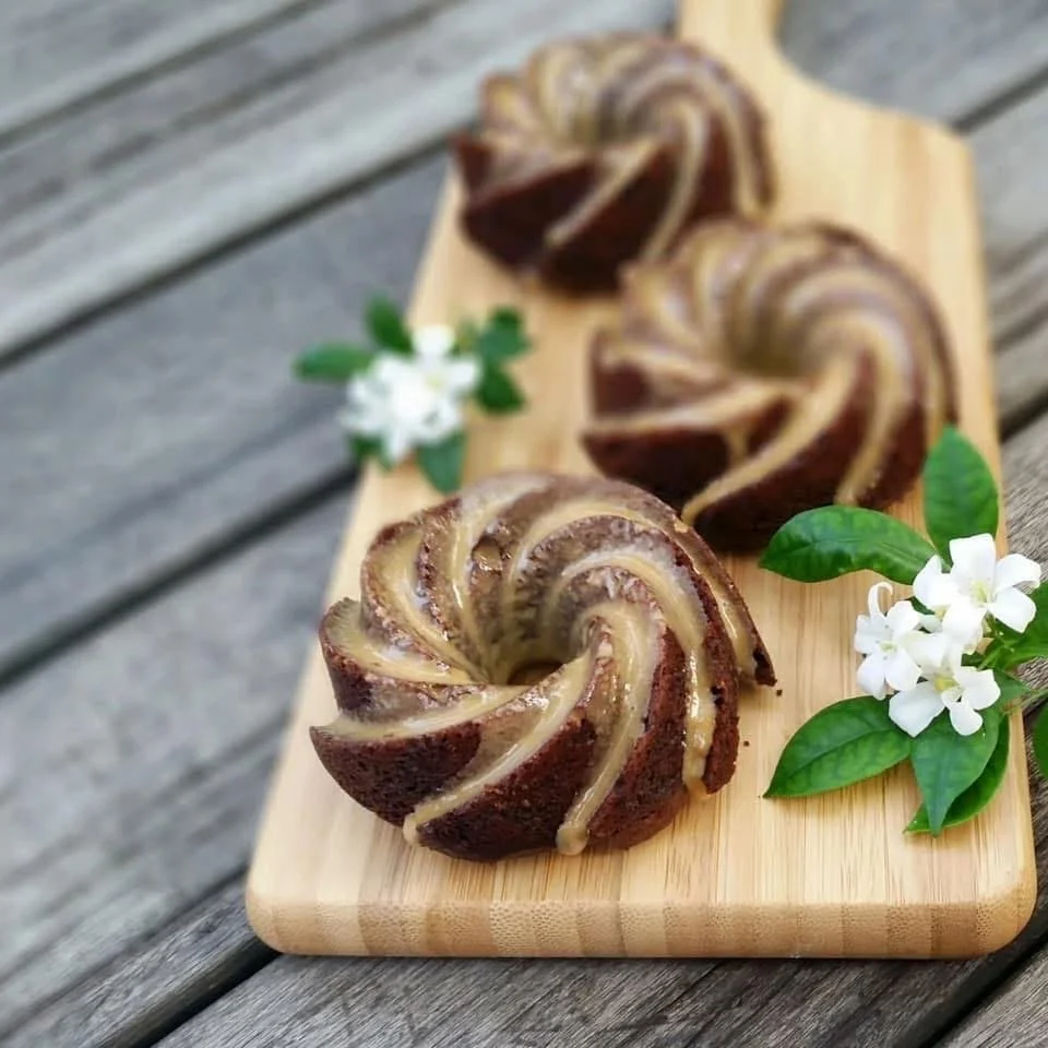 Three swirl-shaped marble cakes on a wooden board, garnished with white flowers and green leaves, on a wooden surface.