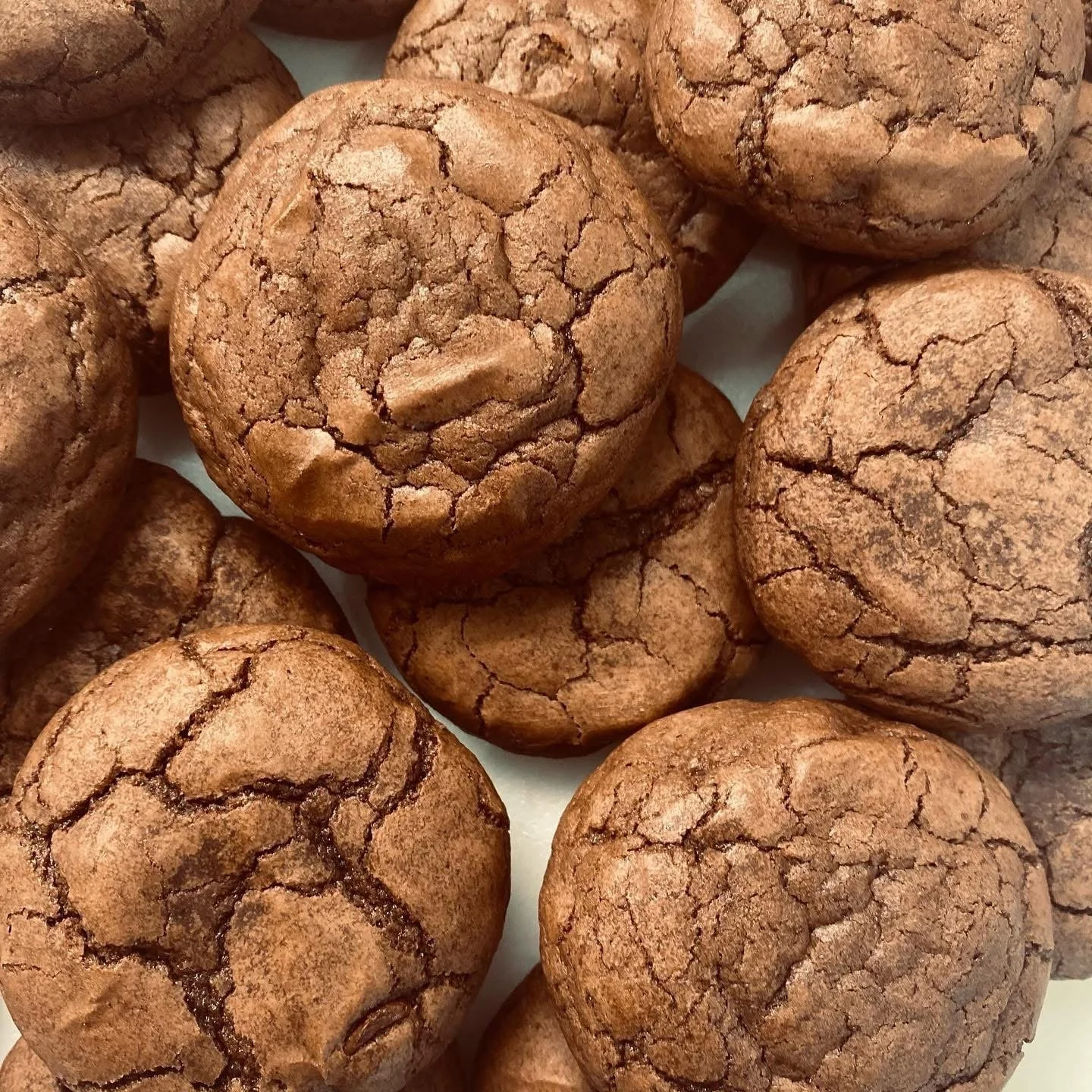Close-up of several round chocolate cookies with cracked tops, arranged on a surface.