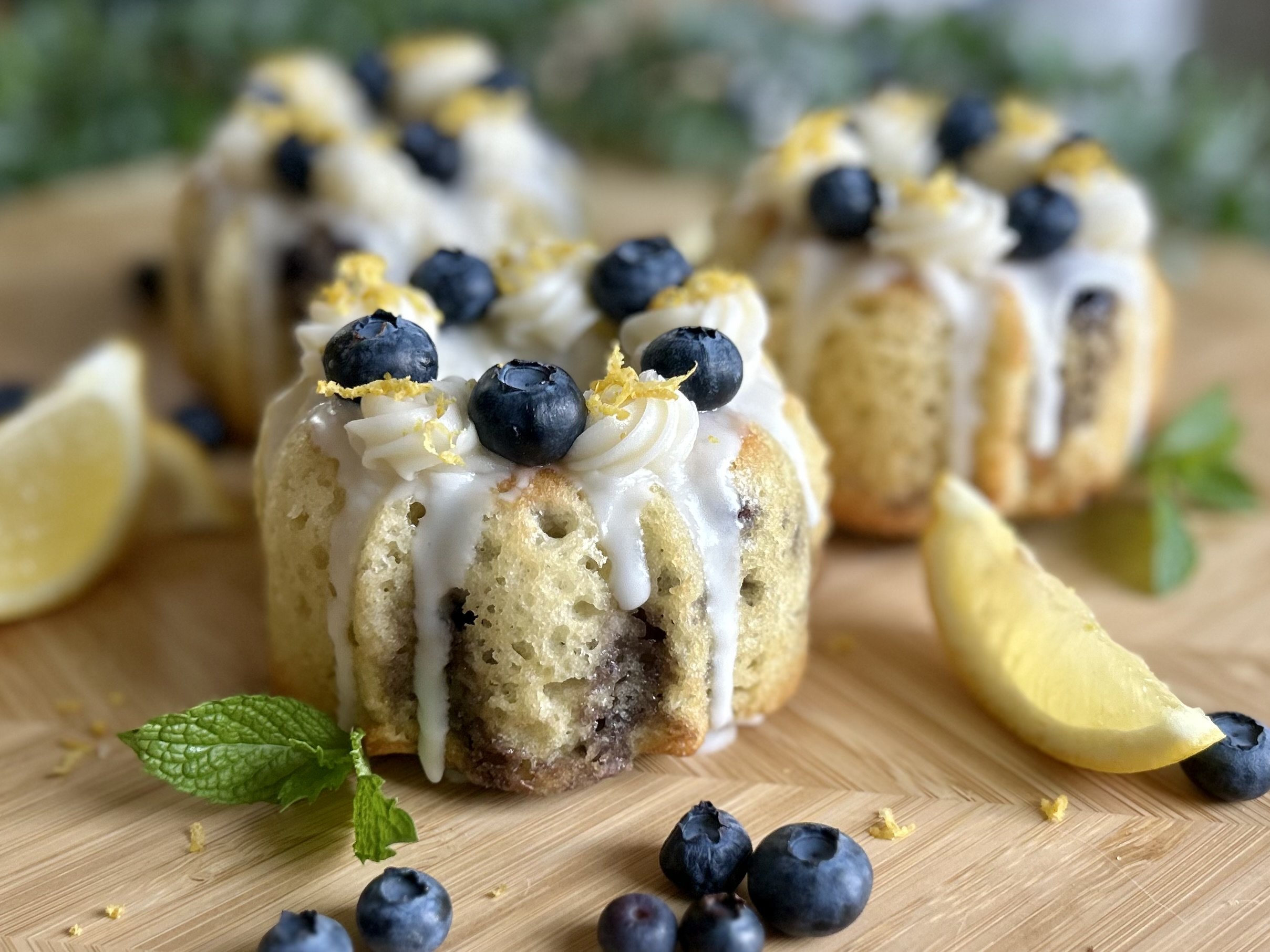 Mini blueberry lava cakes topped with whipped cream and blueberries, served on a wooden board with lemon wedges and mint leaves.
