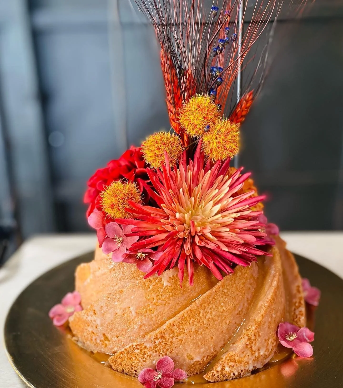 A plated dessert garnished with vibrant colorful edible flowers, including red, yellow, purple, and pink flowers, on a dark plate.