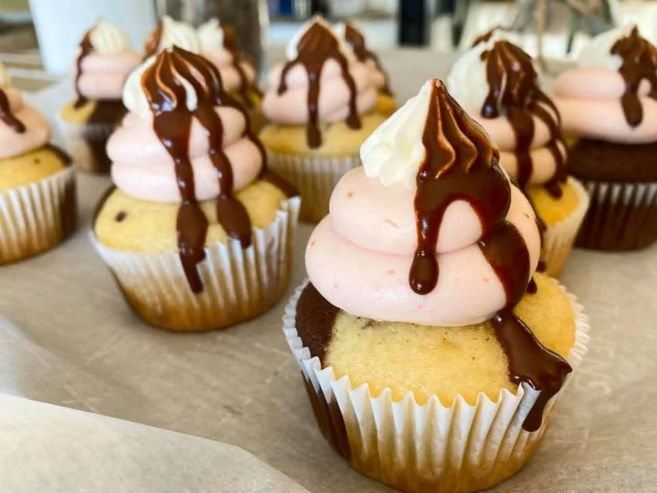 Close-up of our Neapolitan cupcakes topped with strawberry frosting, chocolate drizzle, and a dollop of white frosting.