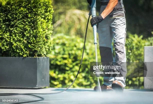 Person using a pressure washer to clean a concrete surface outdoors, South Valley Utah