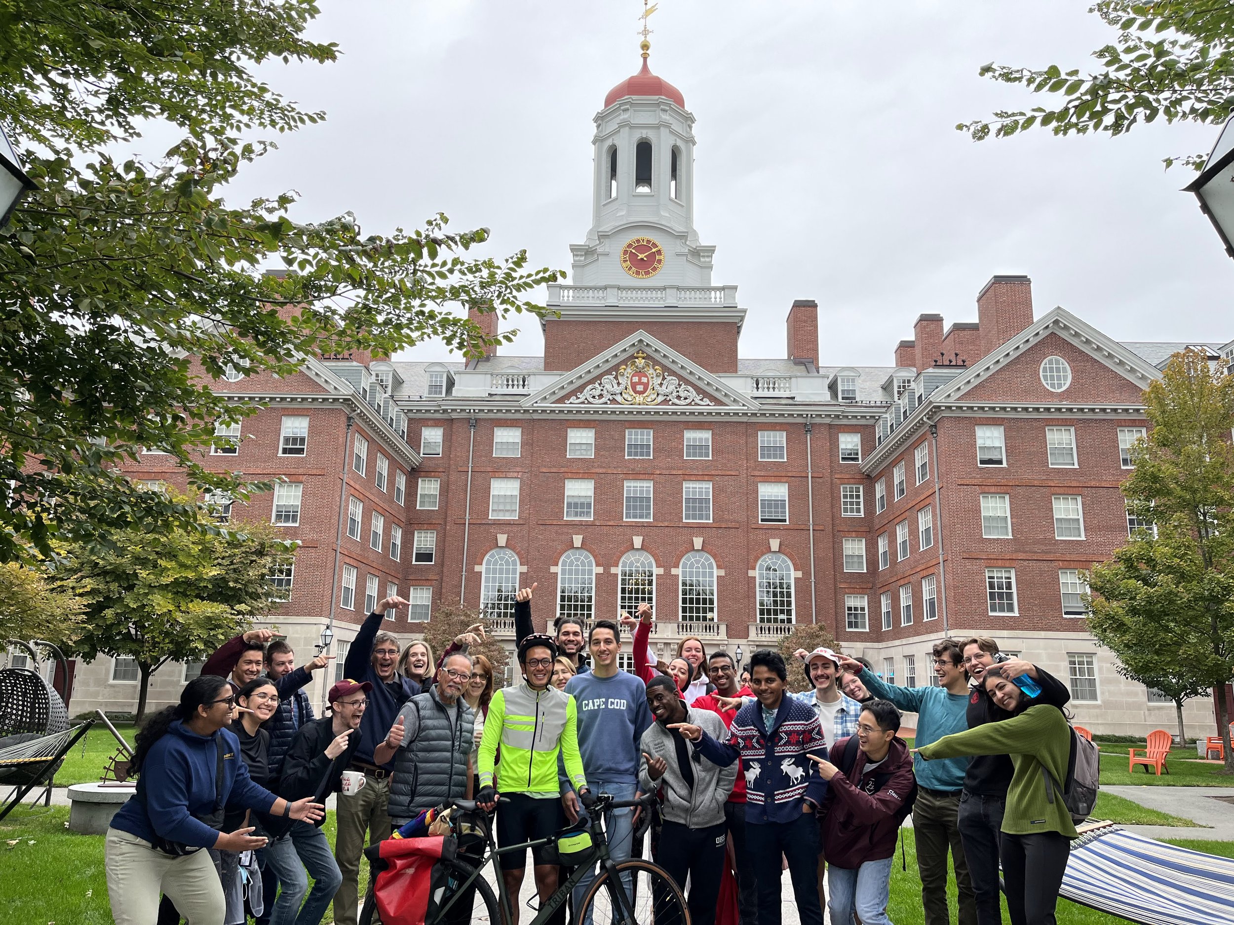 A group of diverse people gathered outdoors in front of a red brick building with a clock tower, smiling and posing for a photo.