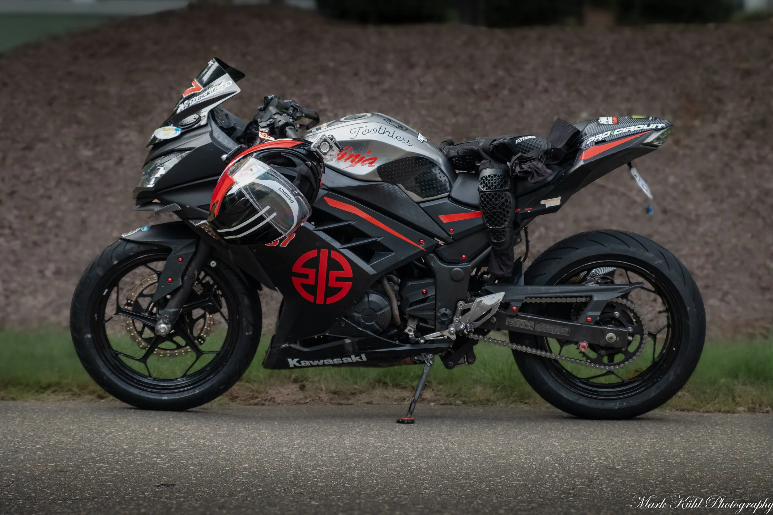 A black Kawasaki sport motorcycle with red and silver accents parked on the street with a black helmet hanging on the handlebar.