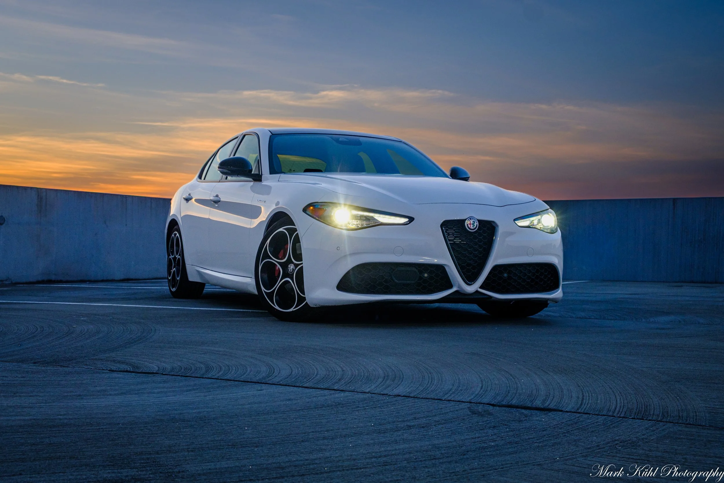 A white Alfa Romeo car parked on a rooftop parking lot during sunset photo shoot