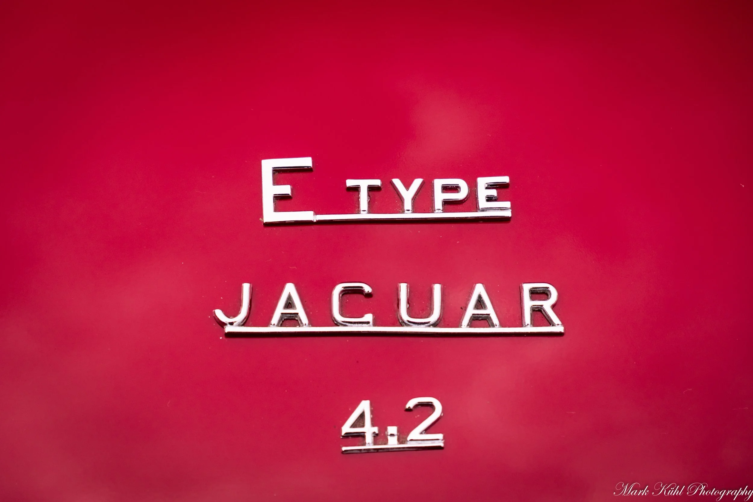 Close-up of car badge with the text 'E TYPE' and the model number '4.2', on a red background.